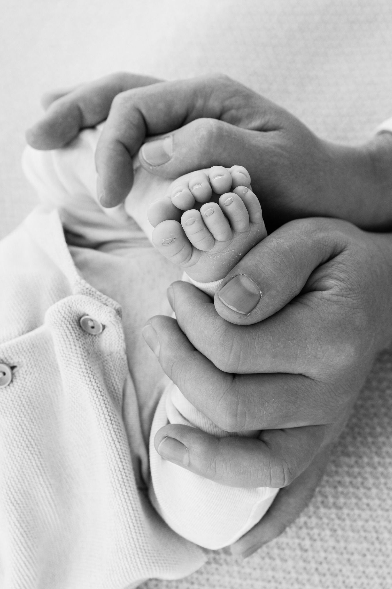 A black and white photo series showing a tiny baby's hand gently holding an adult's finger against a white background.