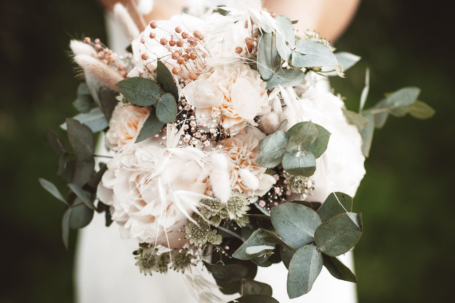 Elegant bridal bouquet with blush roses and eucalyptus against light background.