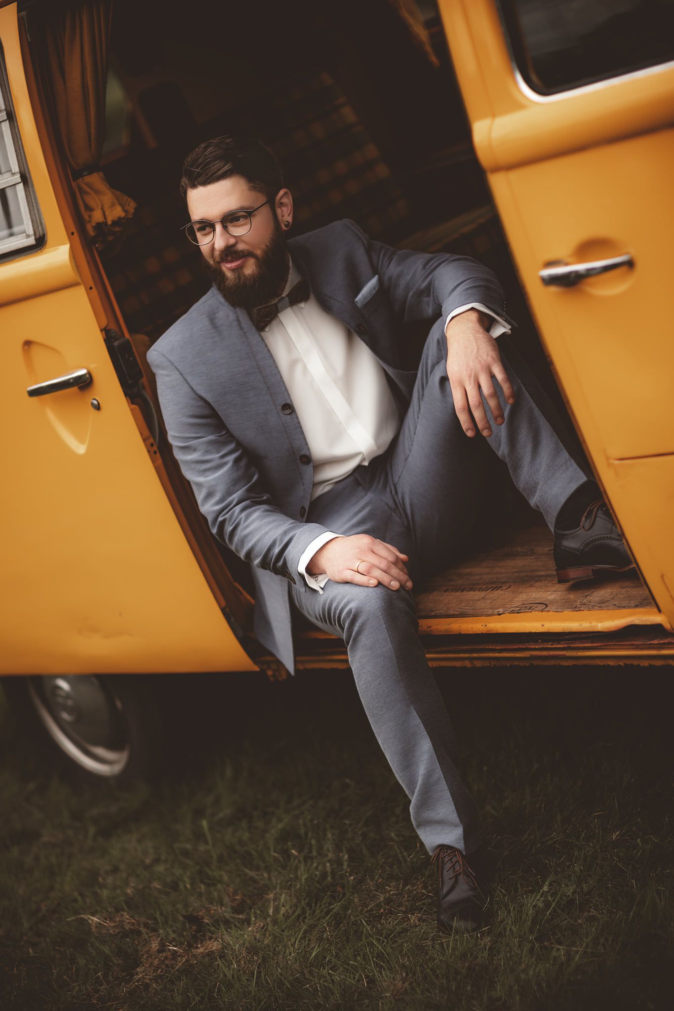 Formal portrait of groom in grey suit seated in yellow vintage van.
