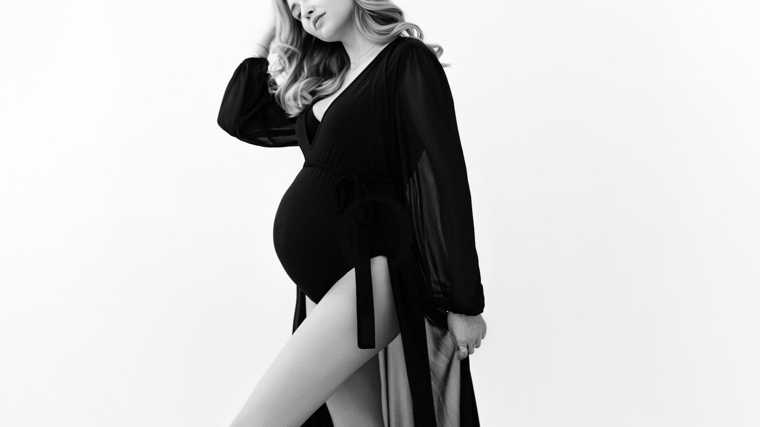 A person in a black dress and high heels poses elegantly against a white background in a fashion photoshoot.