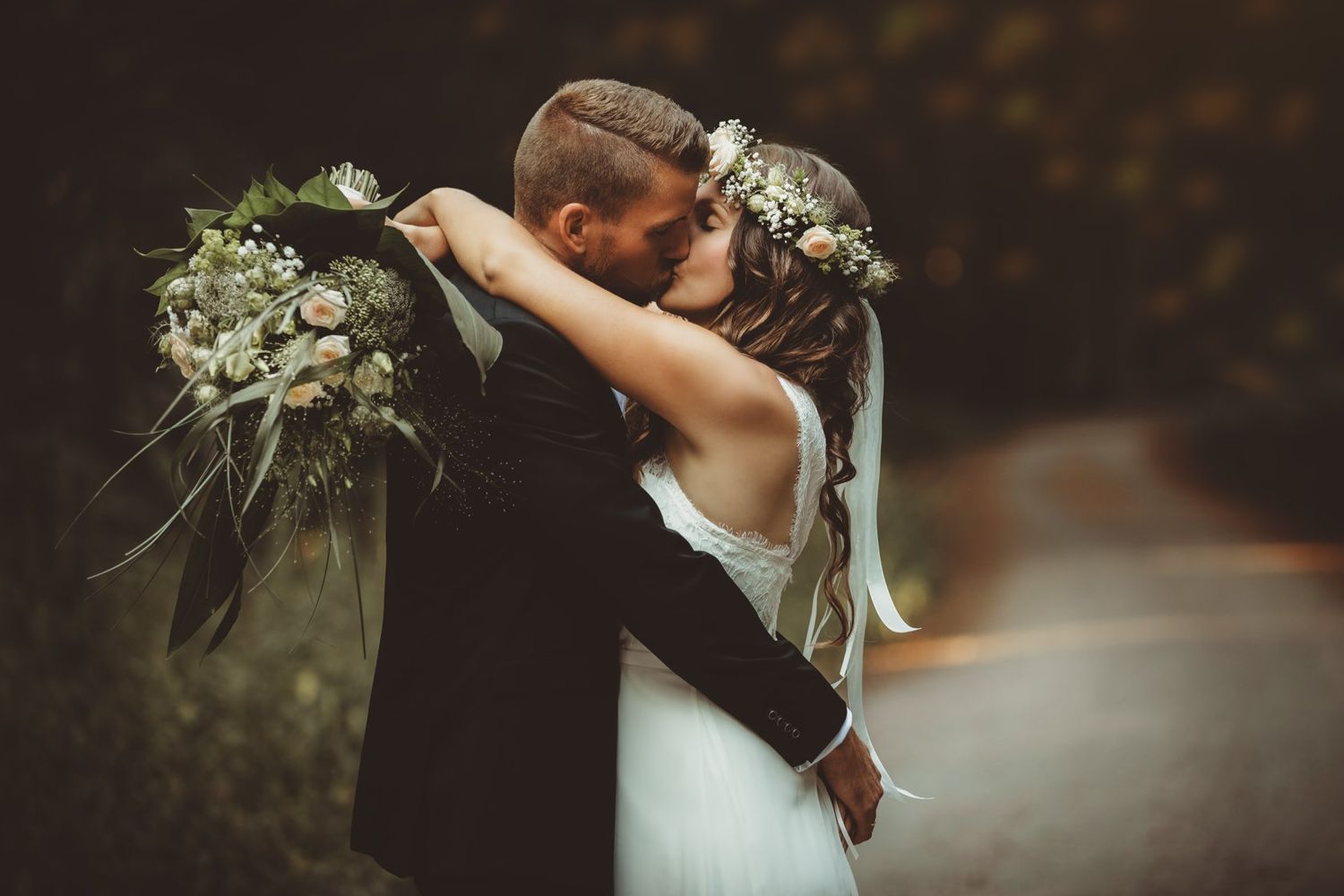 A romantic wedding couple embraces in a rustic outdoor setting with soft lighting.