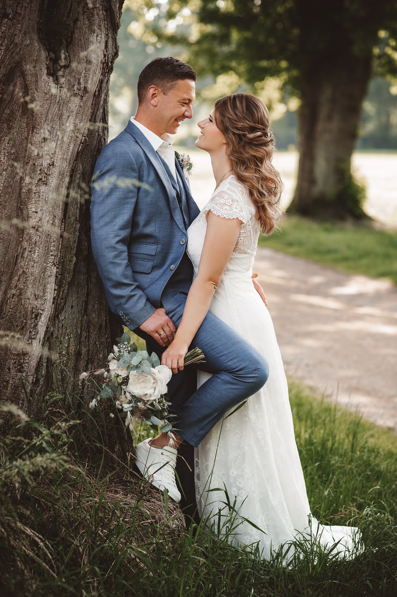 Wedding couple shares intimate moment against tree backdrop in outdoor setting.