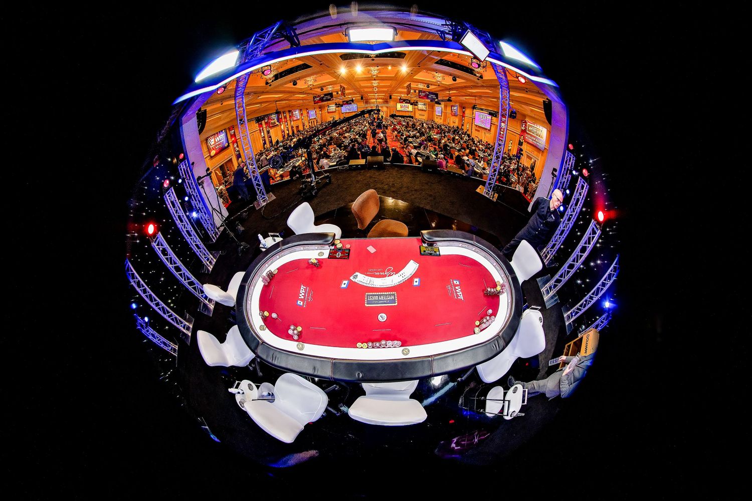 Fisheye lens view of a poker tournament final table in a grand casino hall with spectators.