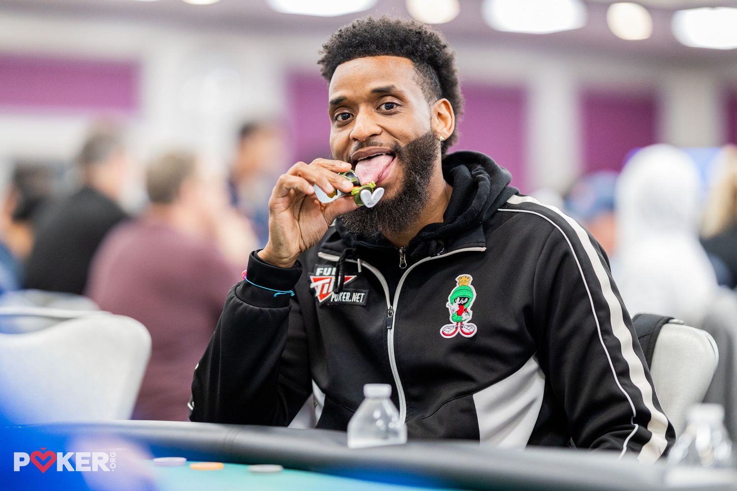 NBA player wearing a black Boston Celtics jacket smiles while biting a poker chip at a gaming table.