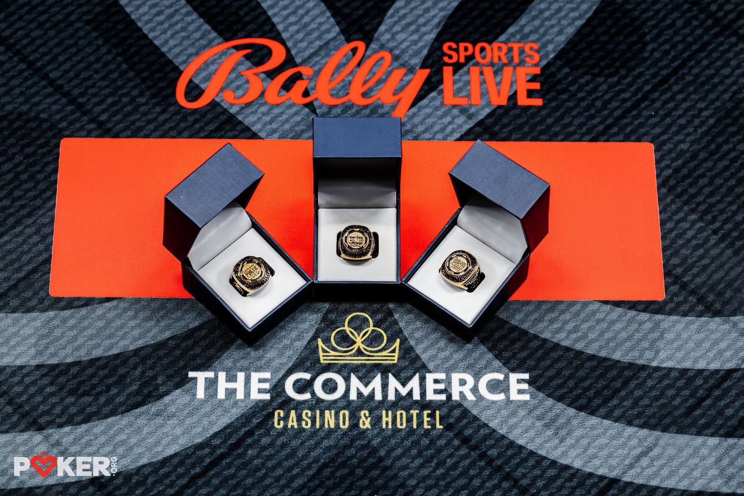 Three World Series championship rings displayed on a red surface with Bally Sports Live and The Commerce Casino branding.