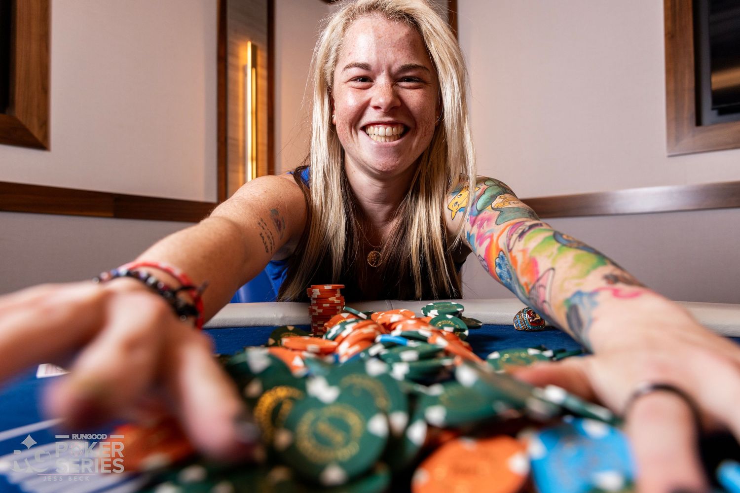 Smiling woman with tattoos reaching for colorful poker chips at a casino card table.