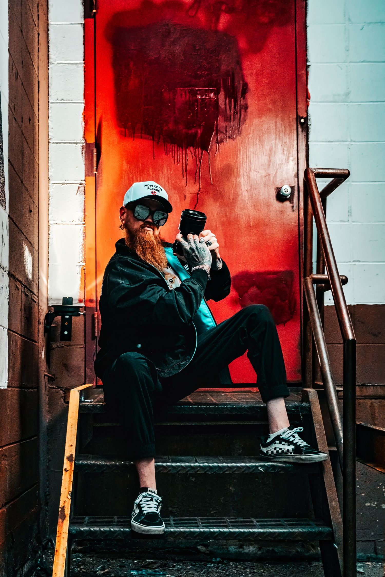 Silhouetted figures stand in dark stairwell illuminated by dramatic red lighting creating moody urban atmosphere.