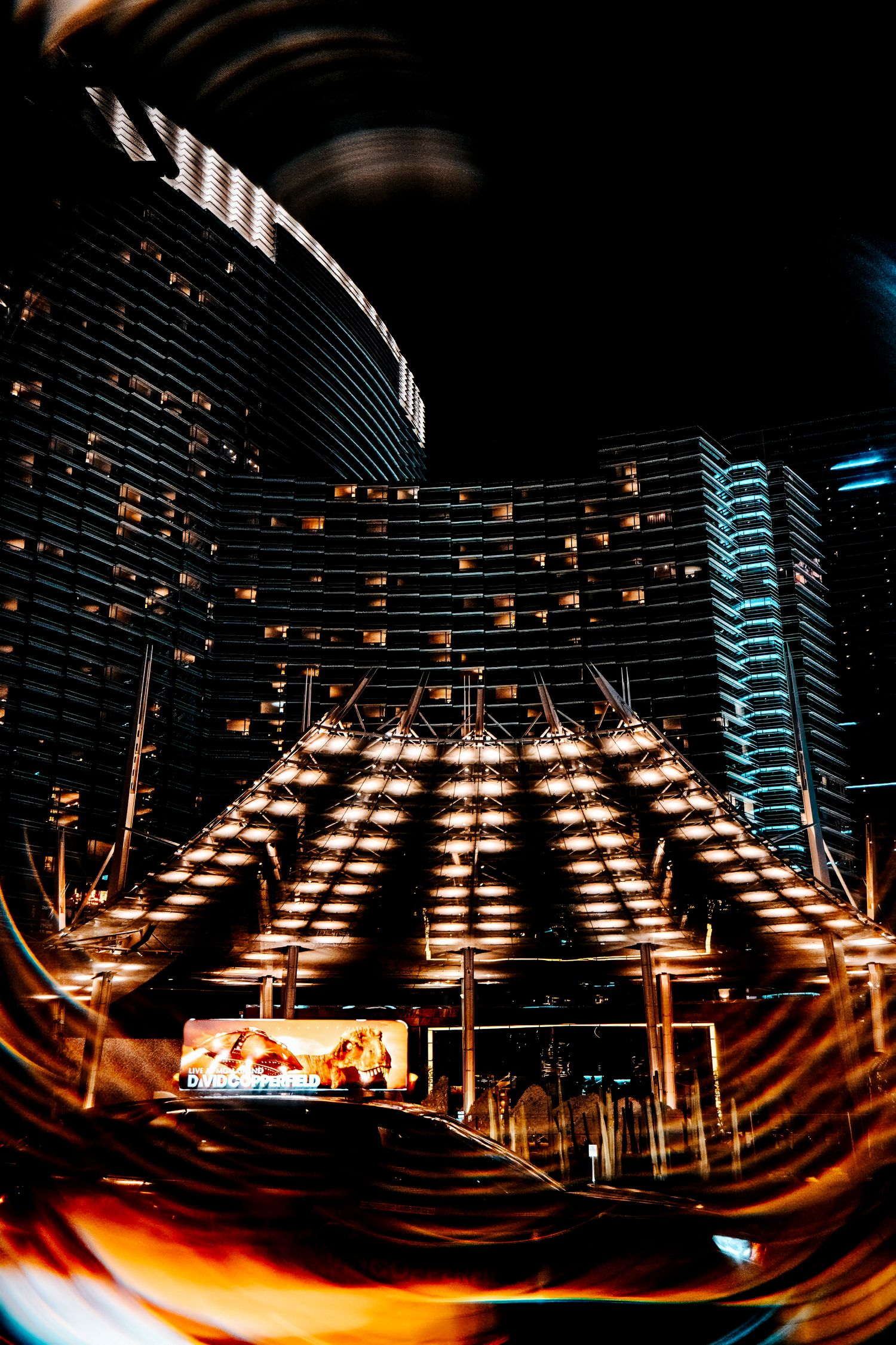 Illuminated modern hotel exterior with curved architecture and rows of lights creating a dramatic nighttime ambiance.