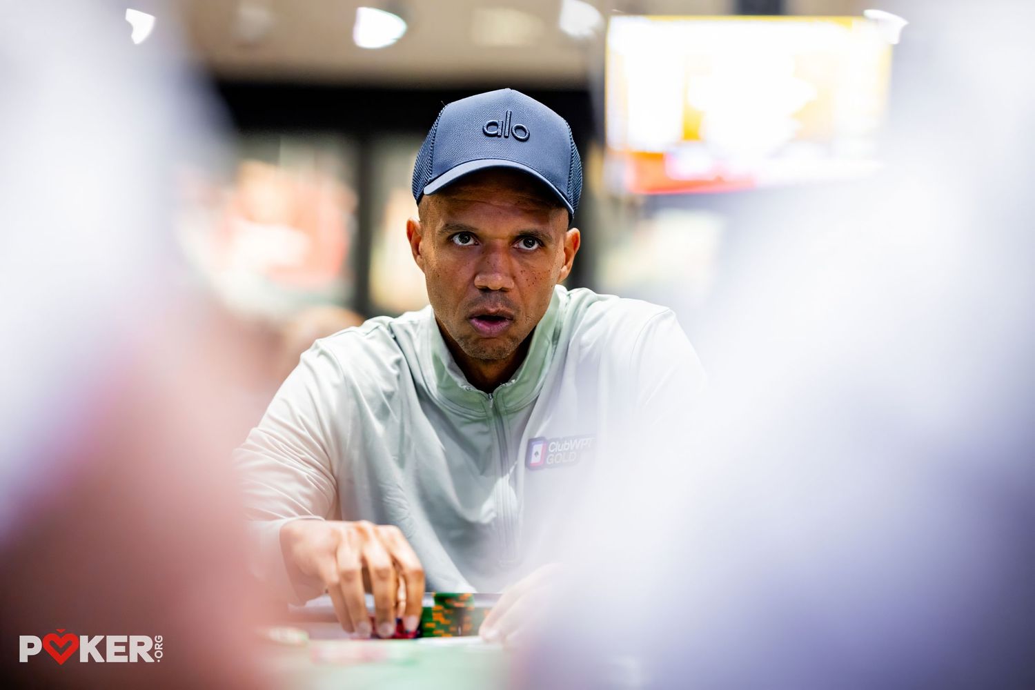 Man in blue cap and white jacket focused at a poker table during a professional tournament.