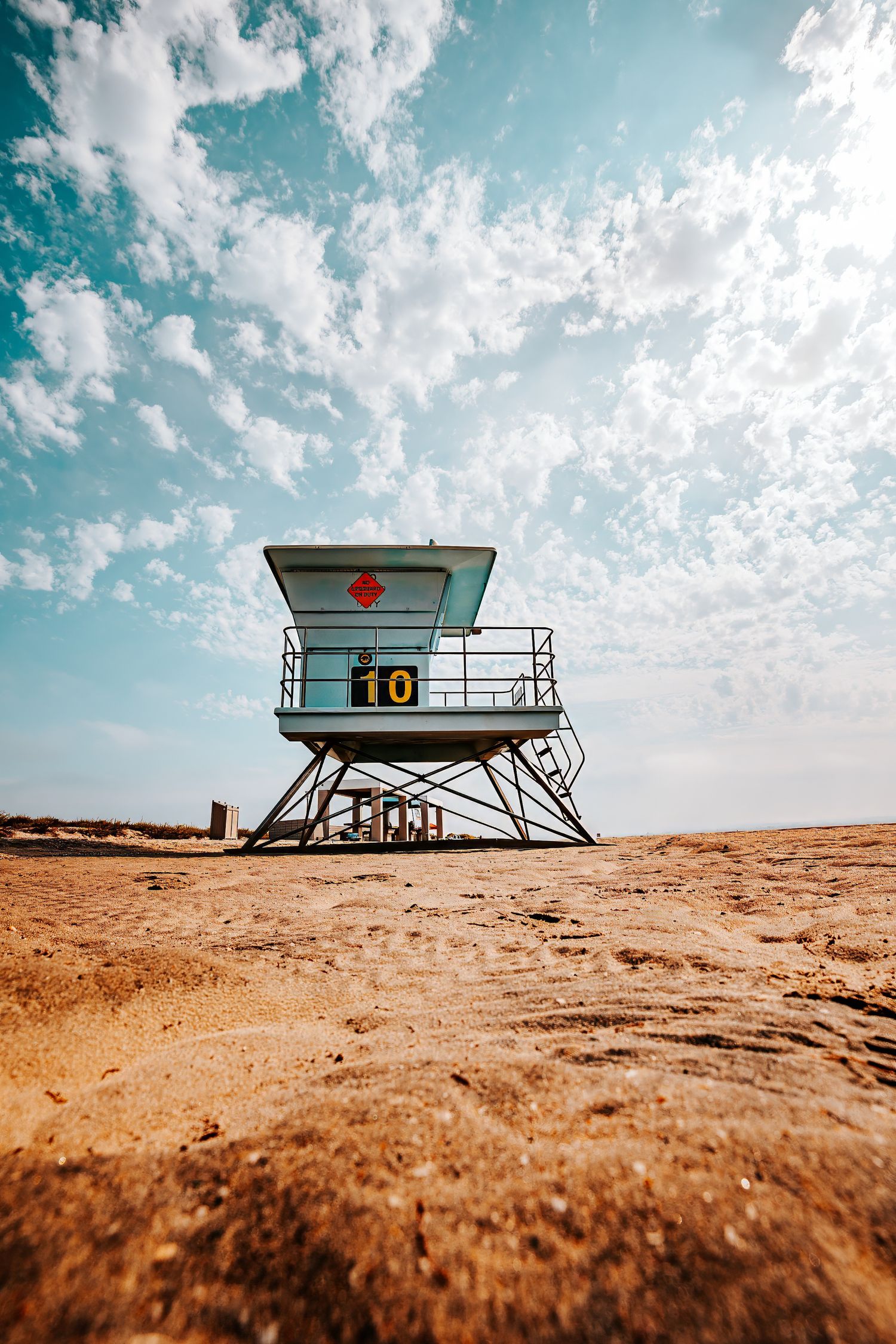 A series of lifeguard towers on a sandy beach under a bright turquoise sky with white clouds.