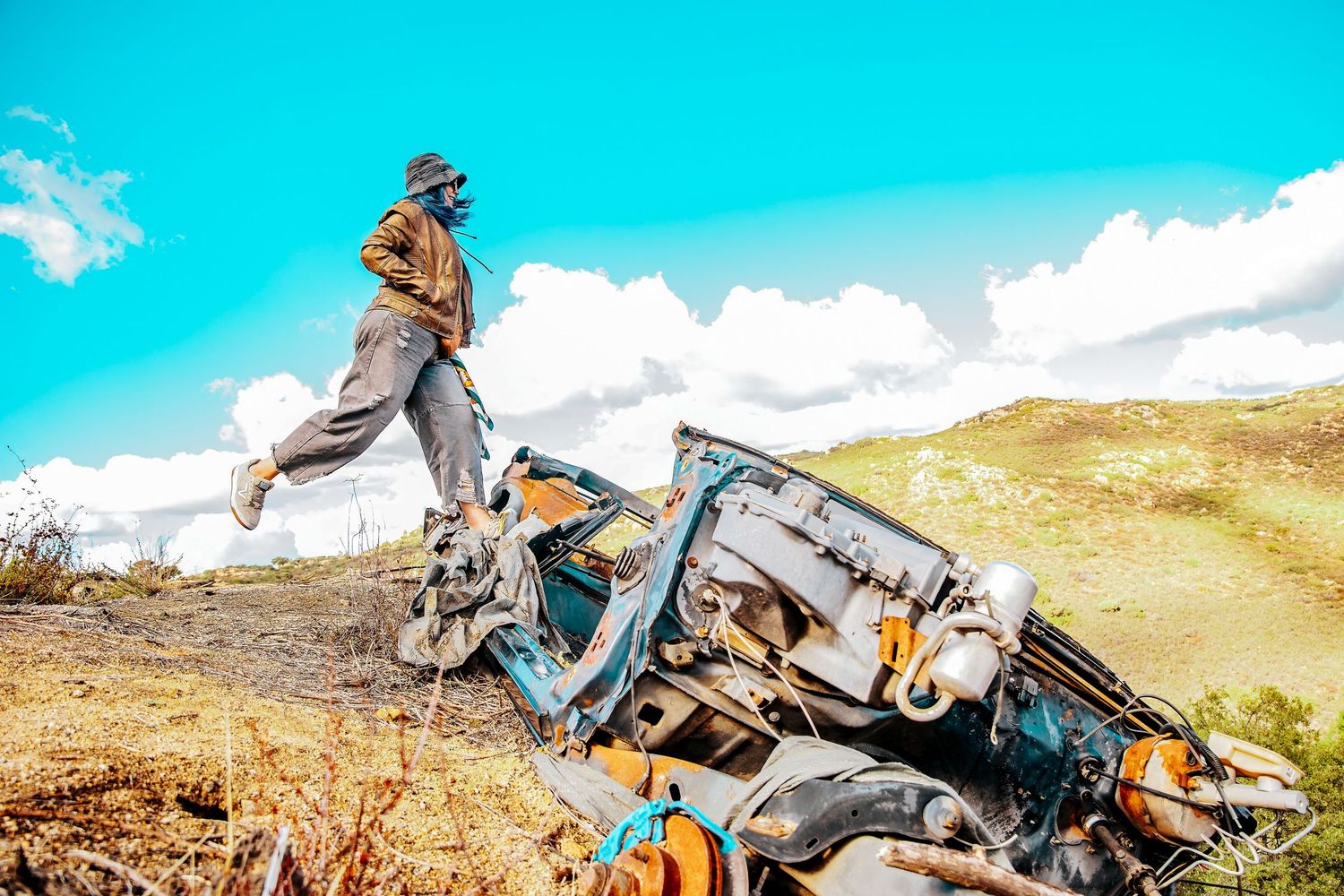 Adventure seeker leaps across rugged mountain terrain with camping gear and backpack against bright turquoise sky.