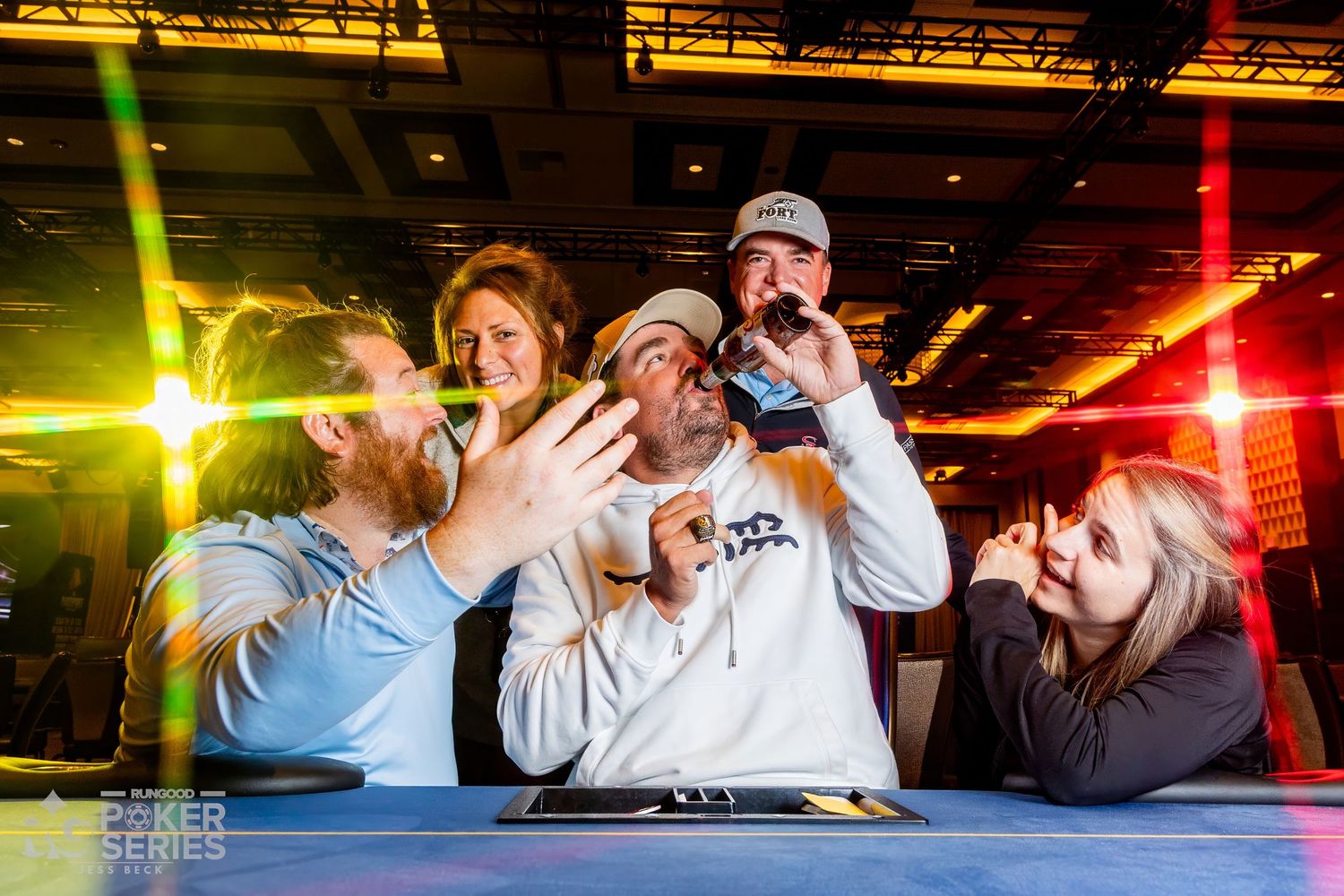 Group of poker players celebrating victory at a Poker Series event, posing excitedly under colorful stage lights.
