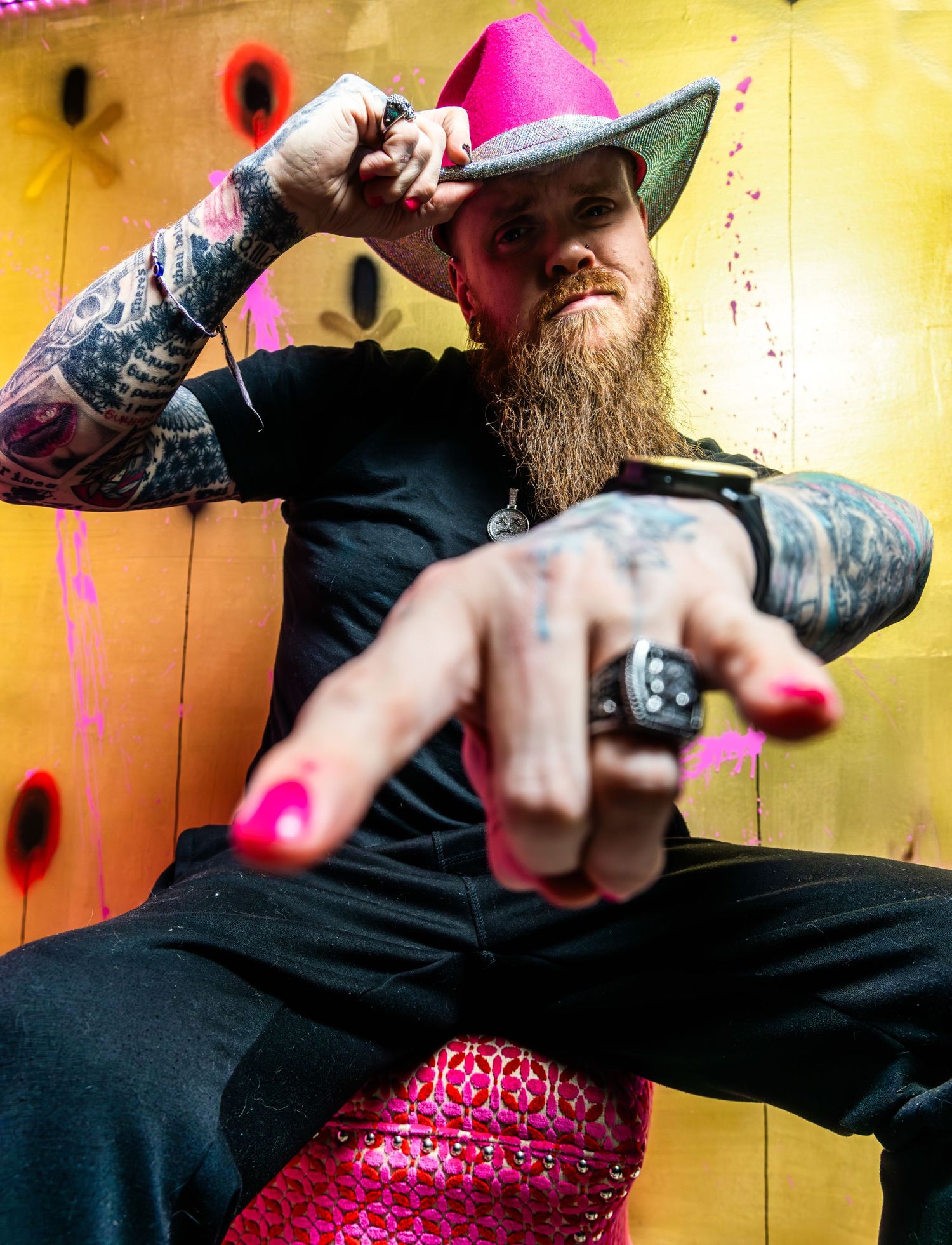 A person in black clothing performs a climbing move on a rock wall with pink and yellow holds.