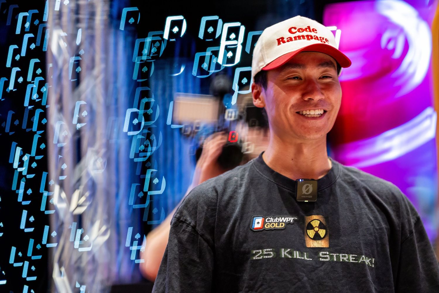Smiling man wearing a red Code Rampant cap and 25 Kill Streak shirt at a gaming event.