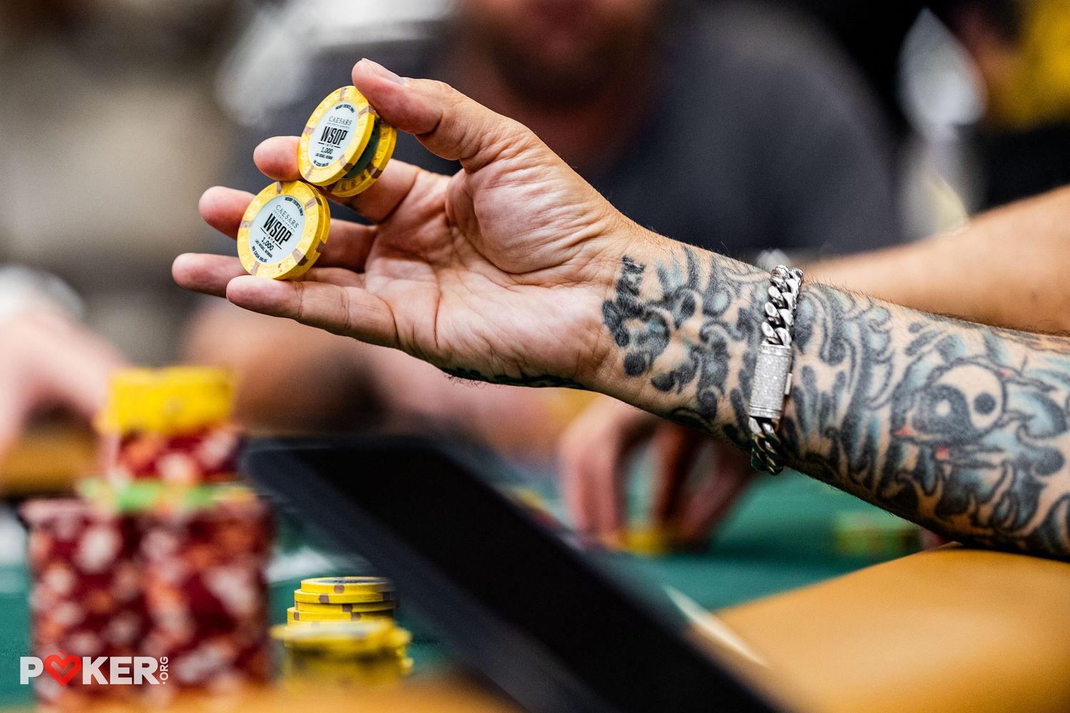 Tattooed hand holding casino poker chips at a WSOP poker tournament table.