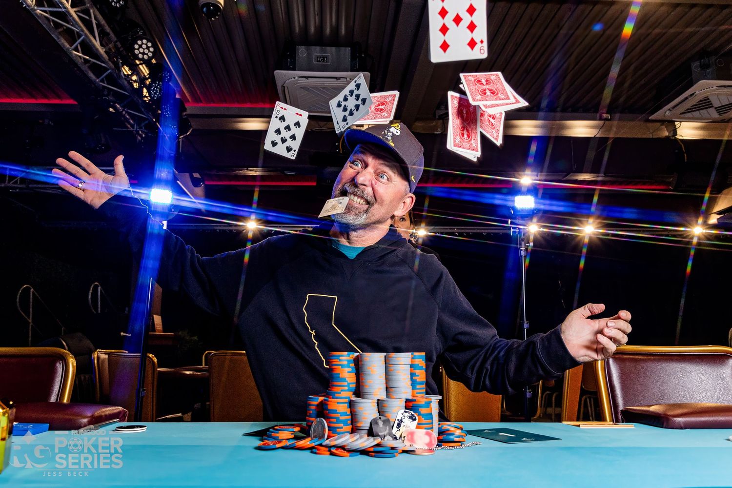 A poker player celebrates a win by tossing cards in the air over a large stack of chips at a poker tournament.