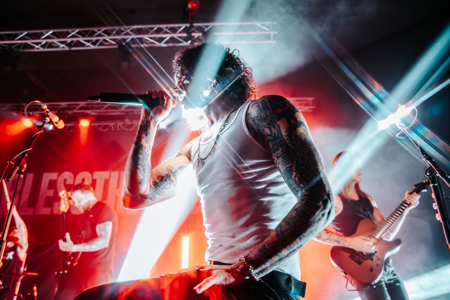 Red and blue lighting illuminates musicians performing on stage during an energetic rock concert performance.