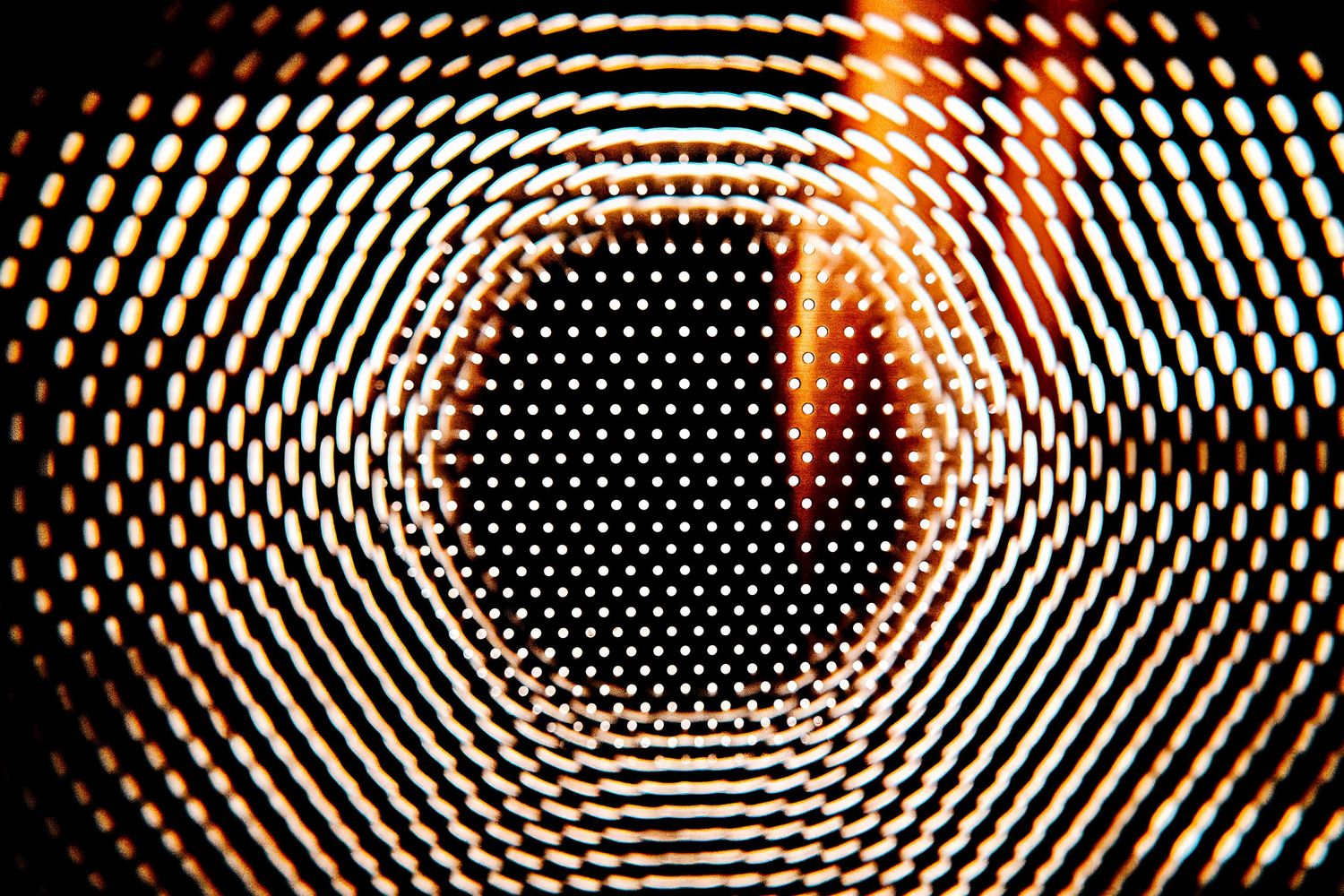 Glowing orange and black hexagonal pattern creating an abstract tunnel effect with concentric circles in darkness.