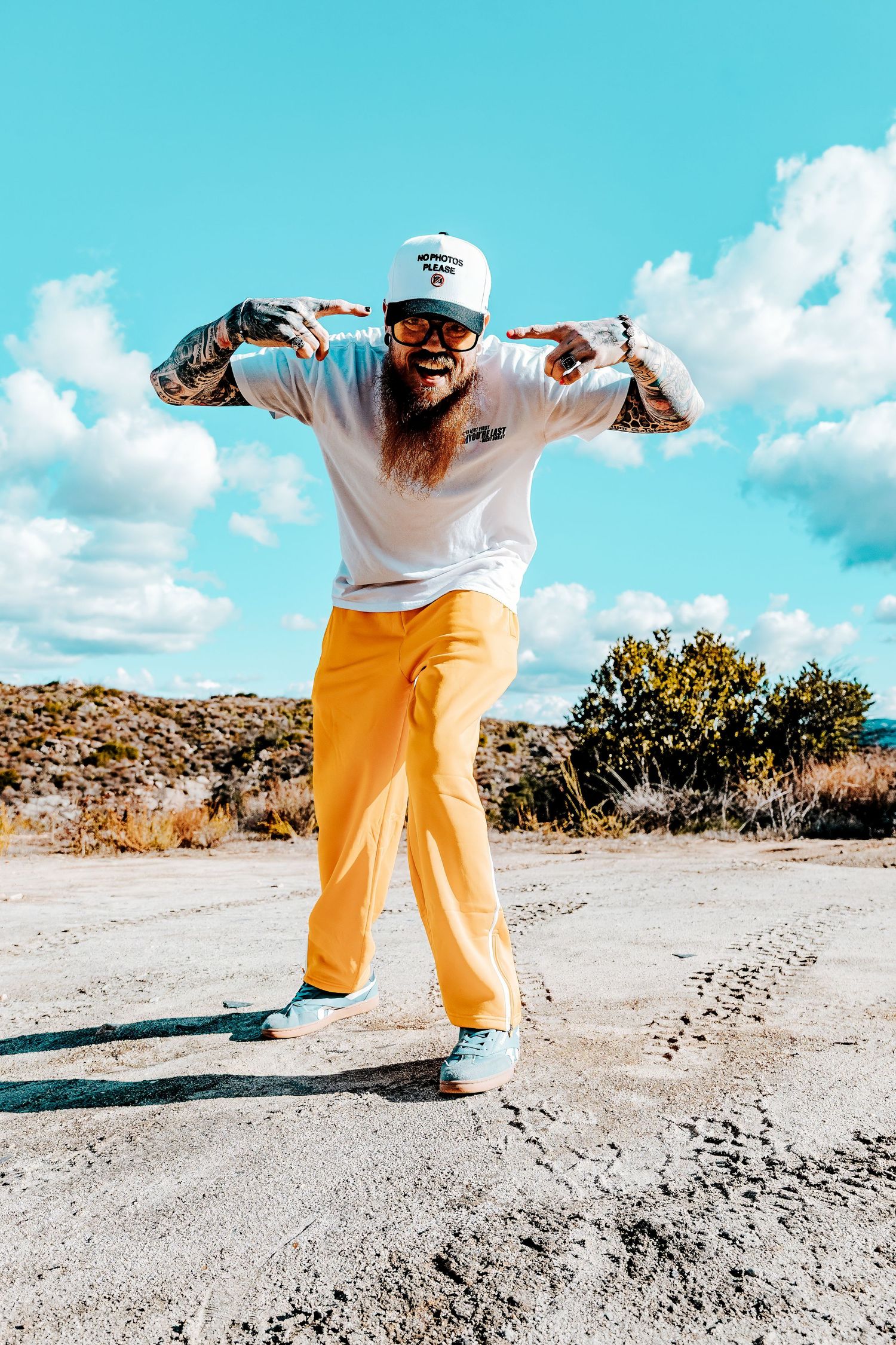 Person in bright yellow pants and white t-shirt poses energetically on a dirt path against blue sky background.