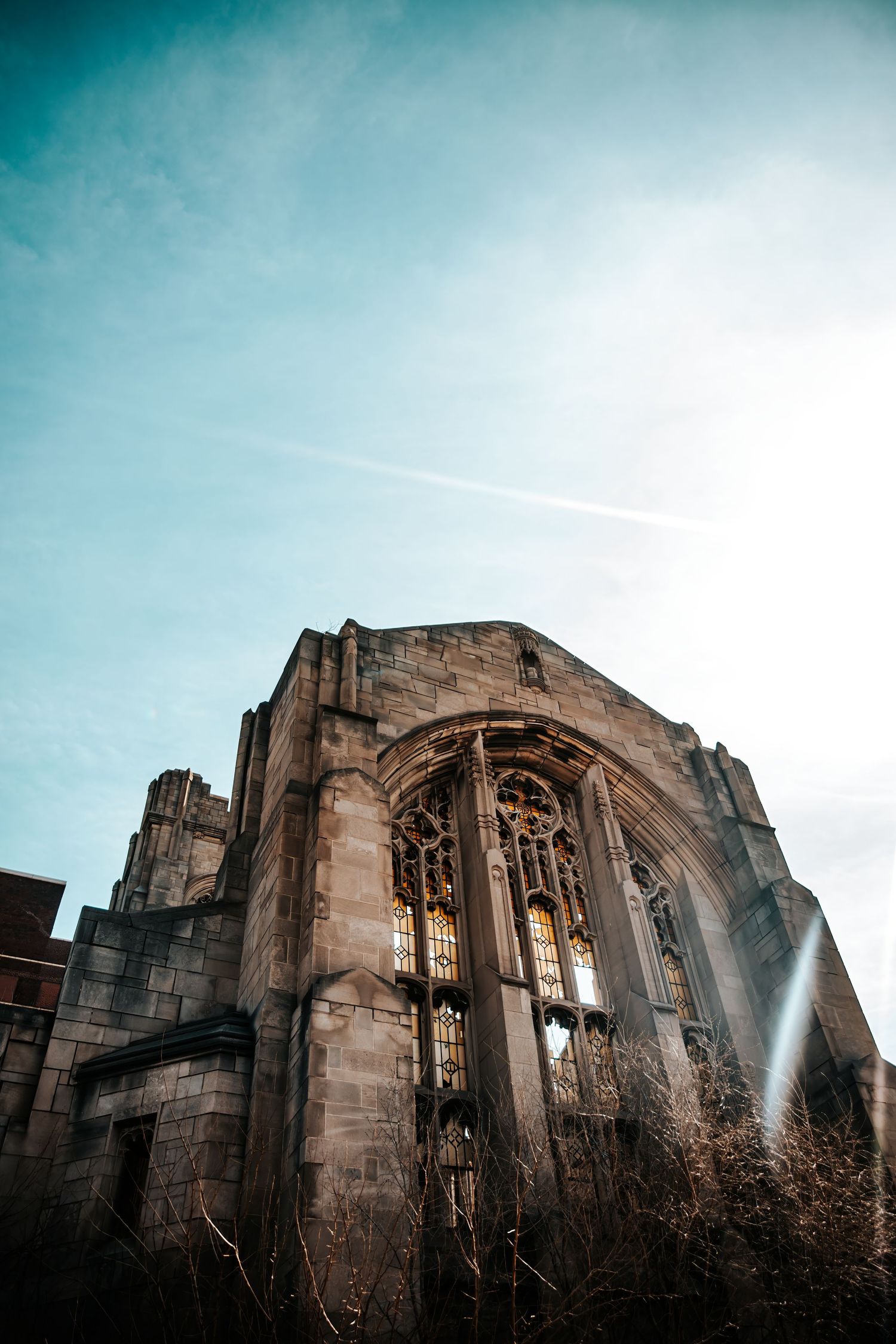 Gothic stone church facade with ornate stained glass windows photographed from below against a blue sky.