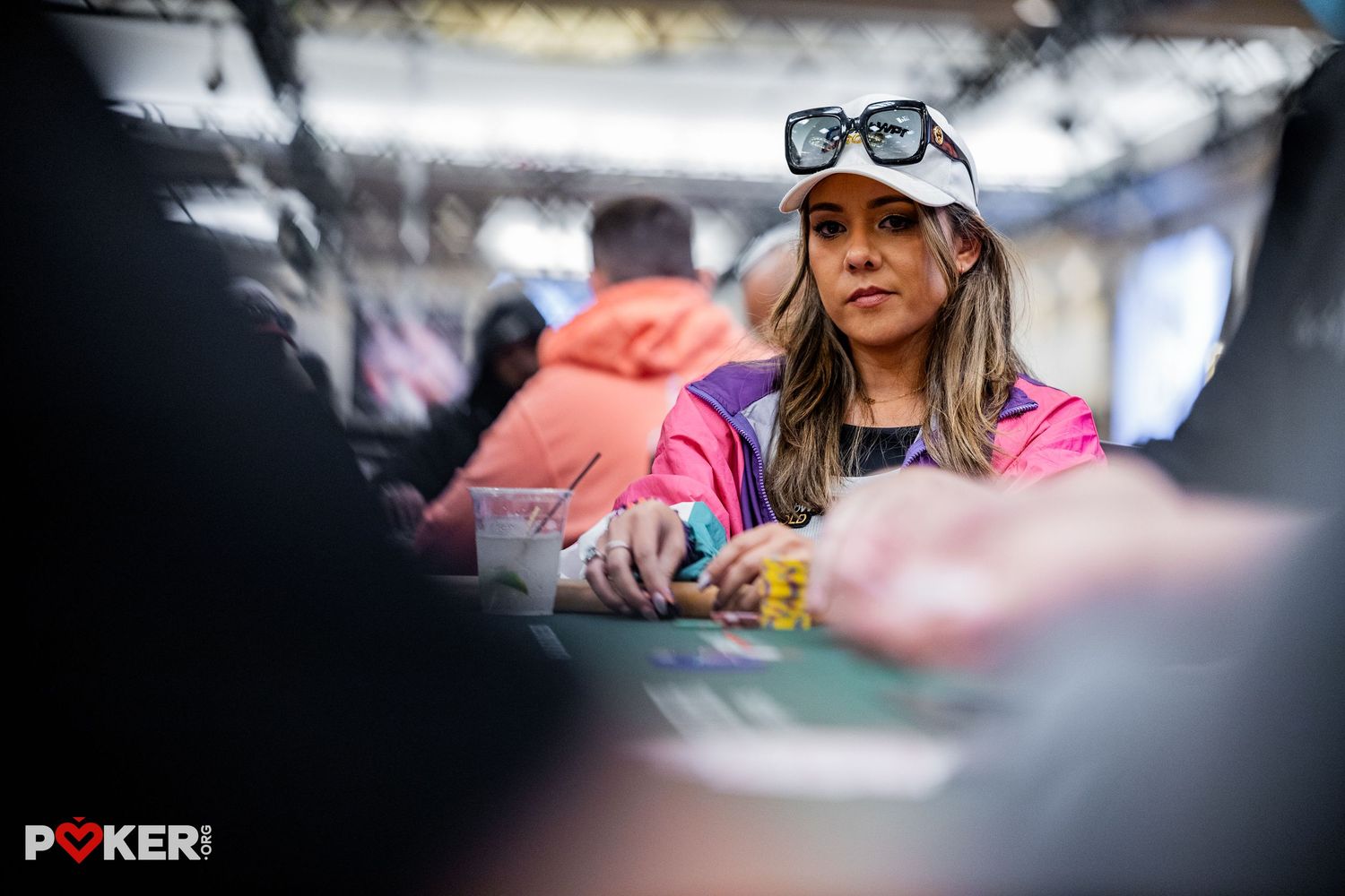 Woman with sunglasses on head playing poker at a casino table during a professional tournament.