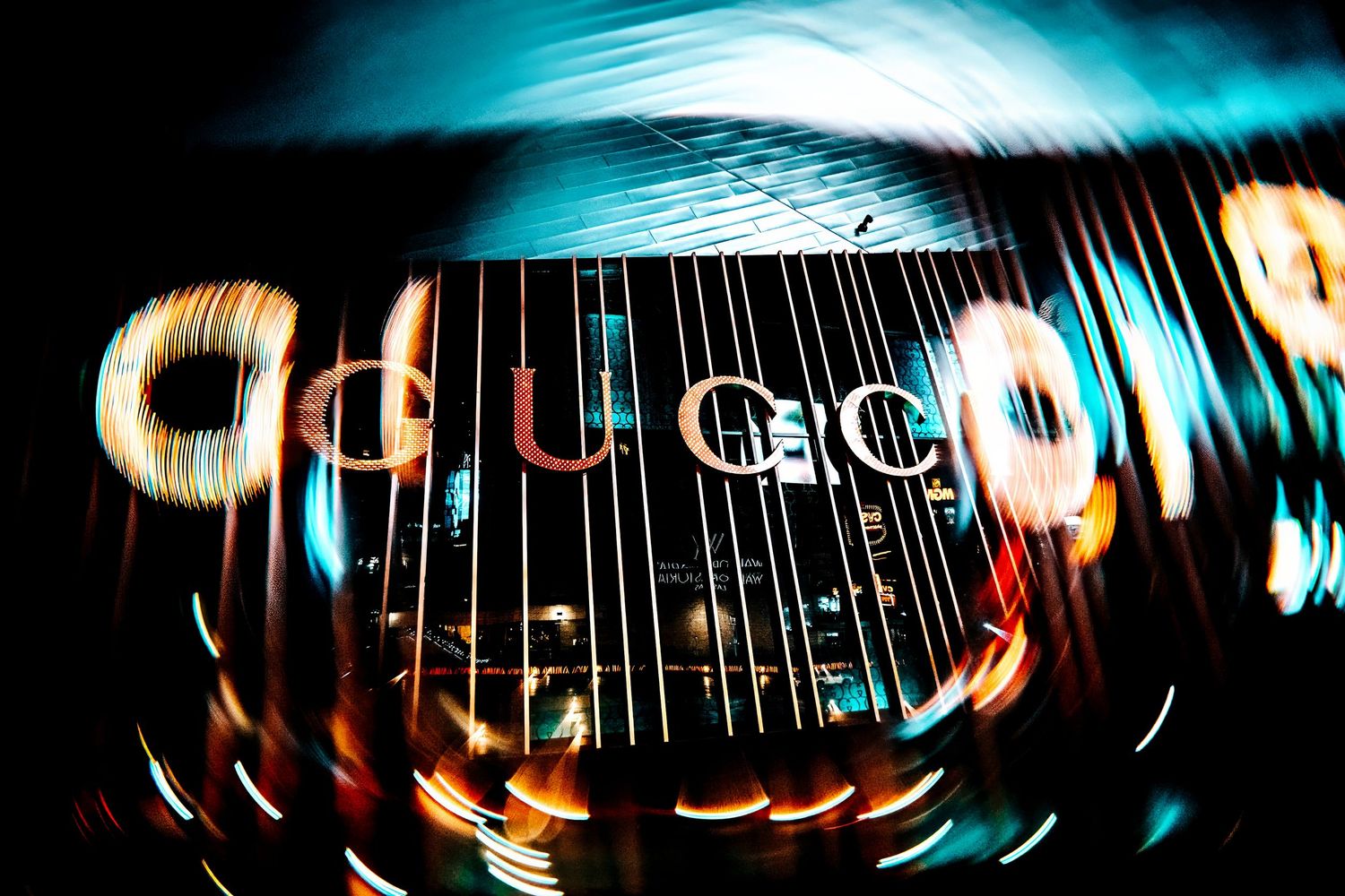 Abstract light blur of Google logo through distorted glass creating a warped neon effect against dark background.