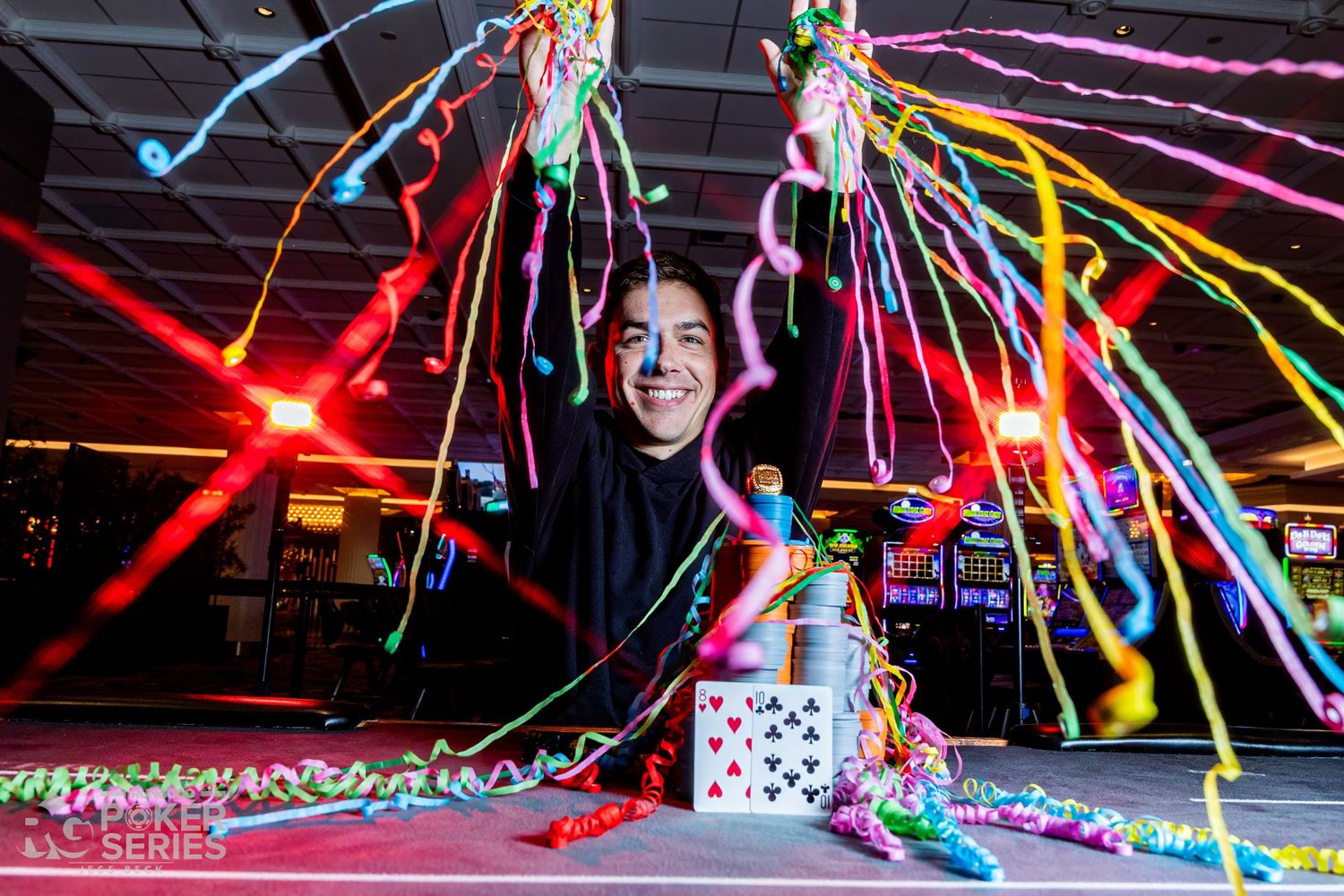Poker player celebrates tournament win with colorful streamers and confetti exploding over a card table at a casino series event.