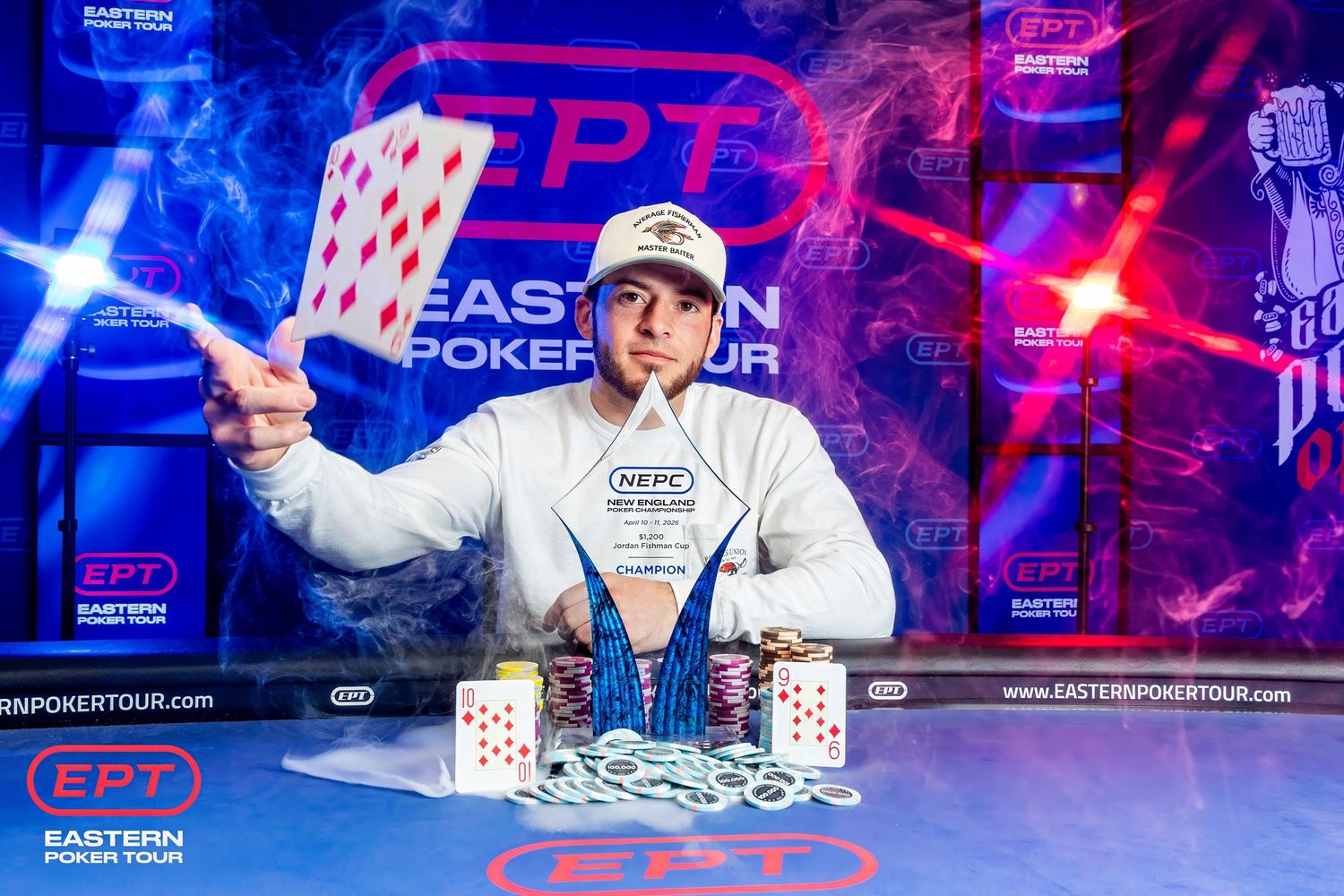 Winner holding playing card at EPT Eastern Poker Tour championship, posing with trophy and chip stacks on stage.