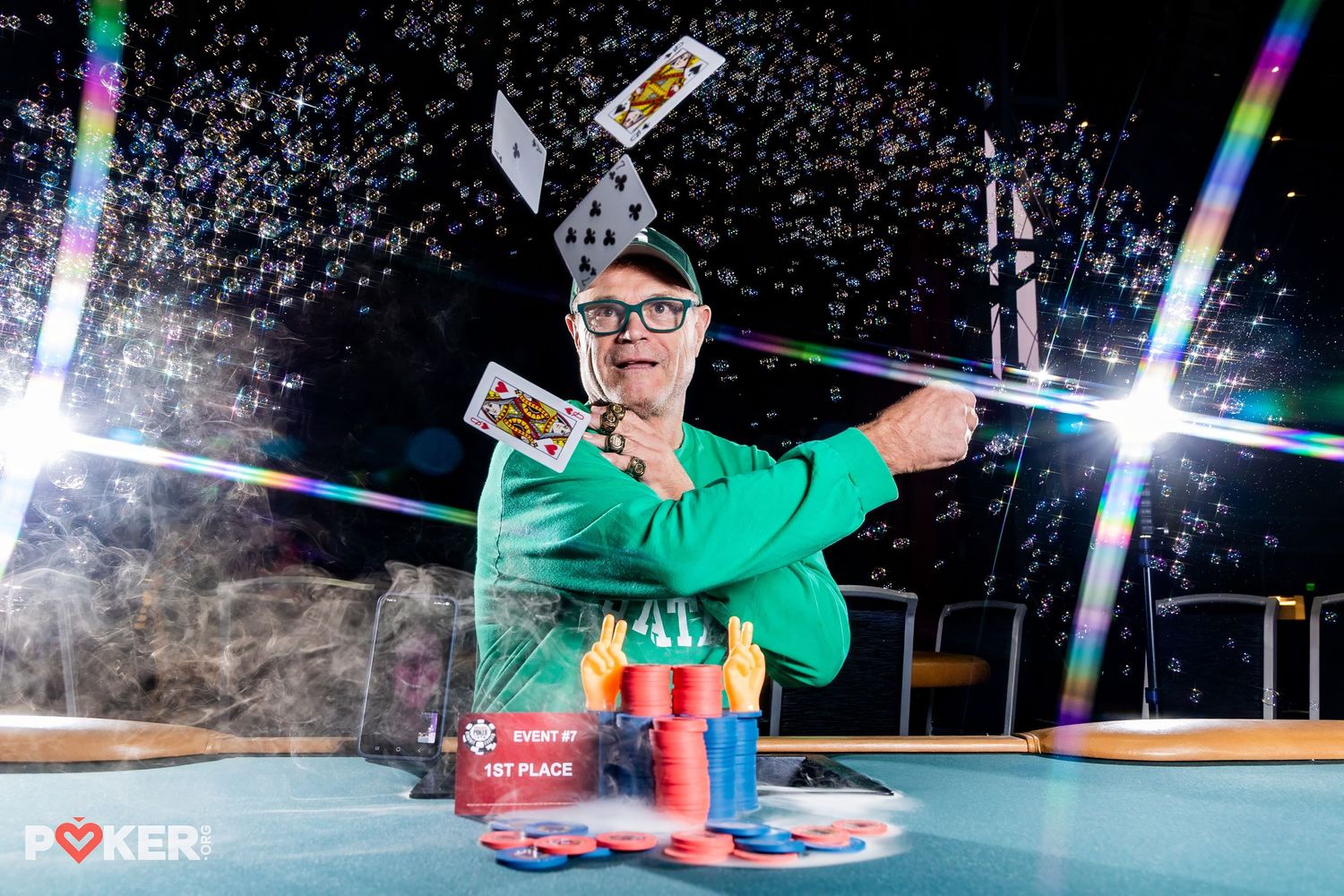 Snowboarder performs aerial tricks at night with colorful lights illuminating the snowy slope.