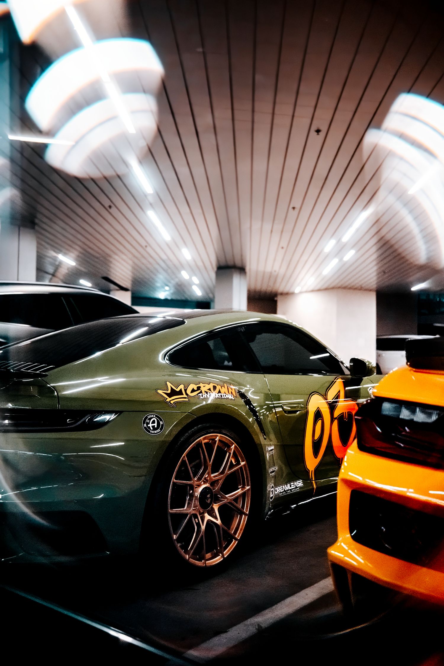 Luxury sports cars parked in modern underground garage with dramatic lighting and custom decals.