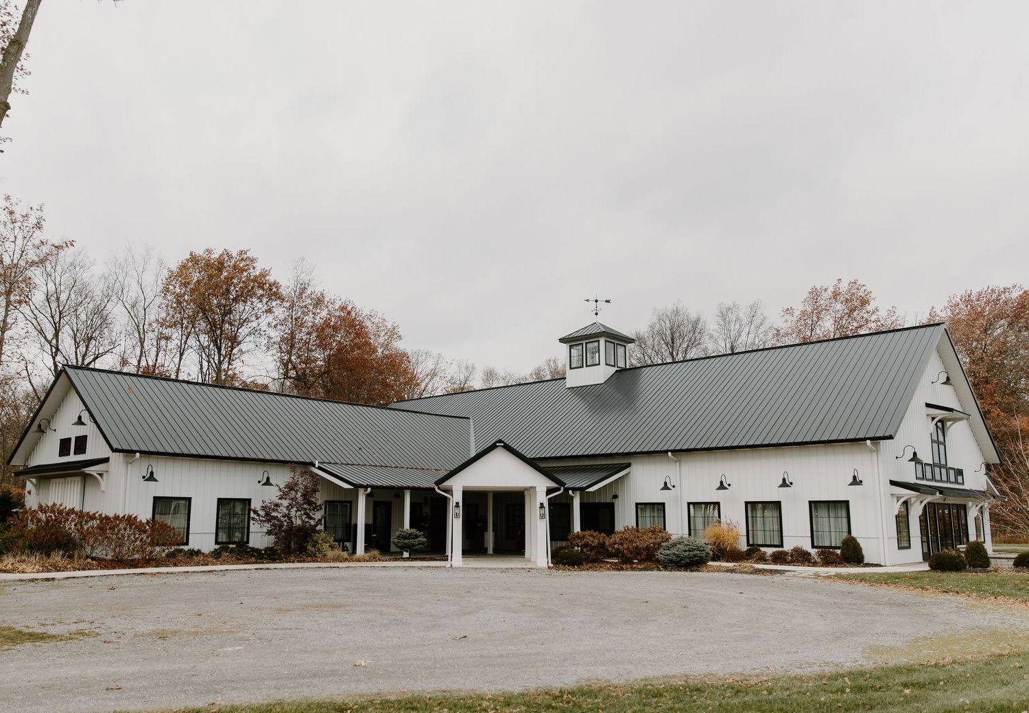 Long white barn-style building with green metal roof sits on a grassy hillside in autumn landscape.