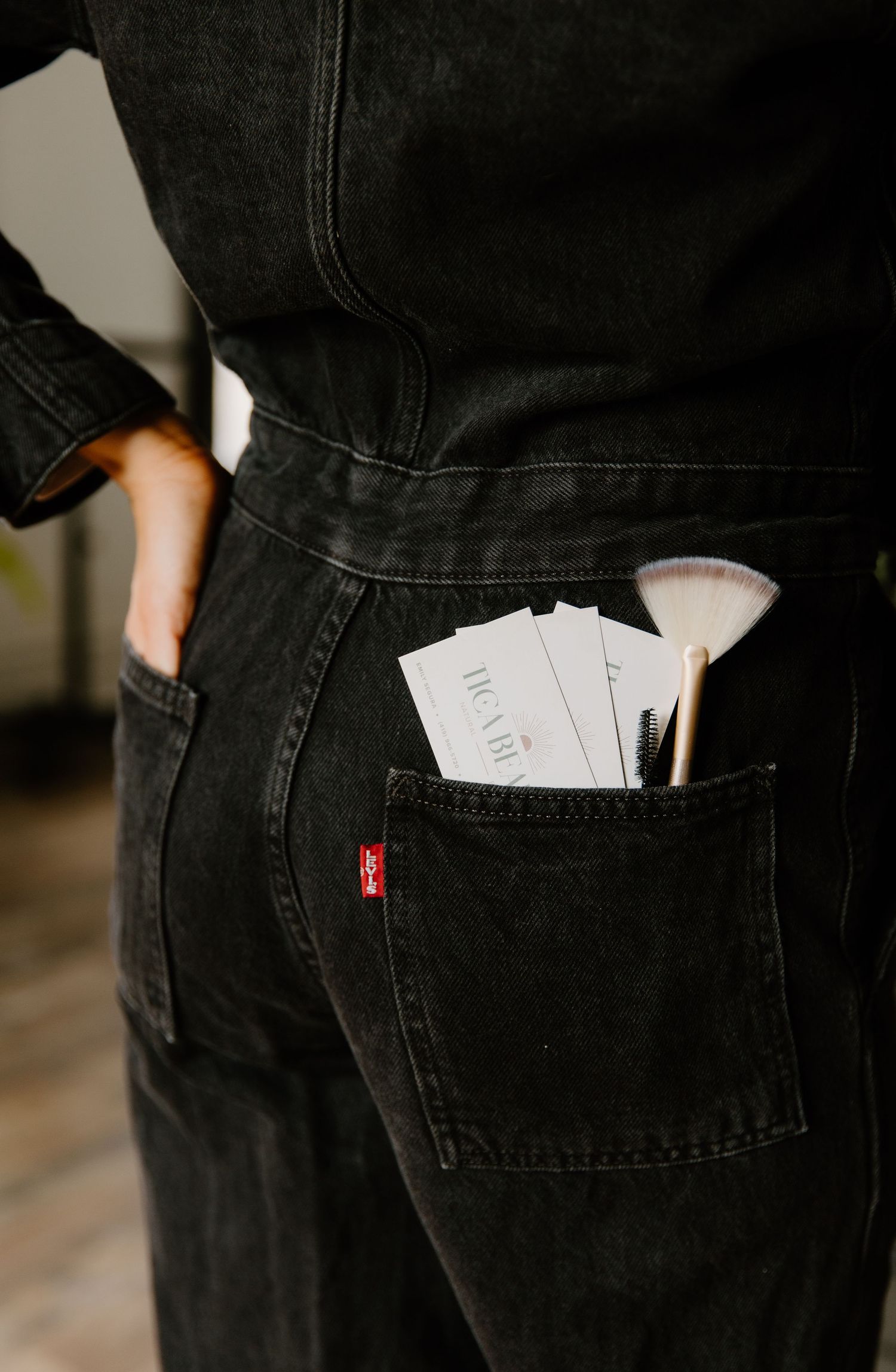Black Levi's denim jeans back pocket holding makeup brushes and business cards.