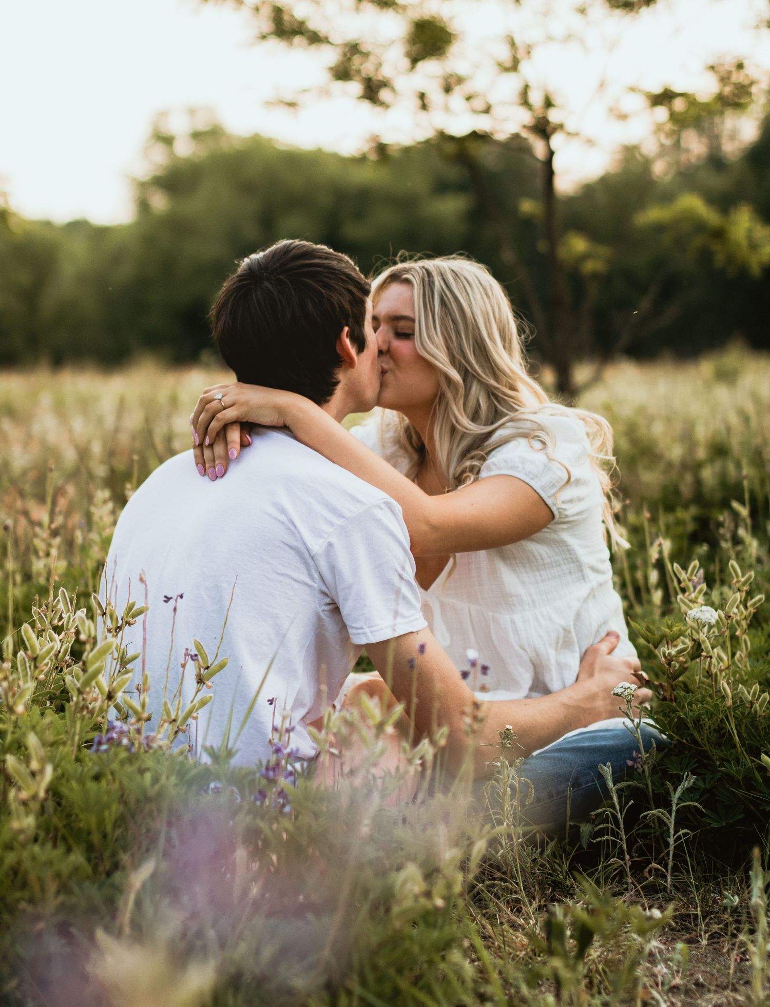 An intimate moment between a couple embracing in a sunlit field of flowers.