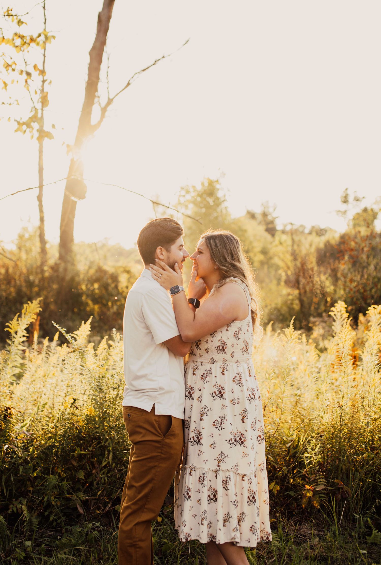 A couple shares a tender moment in a sunlit field with golden grass.