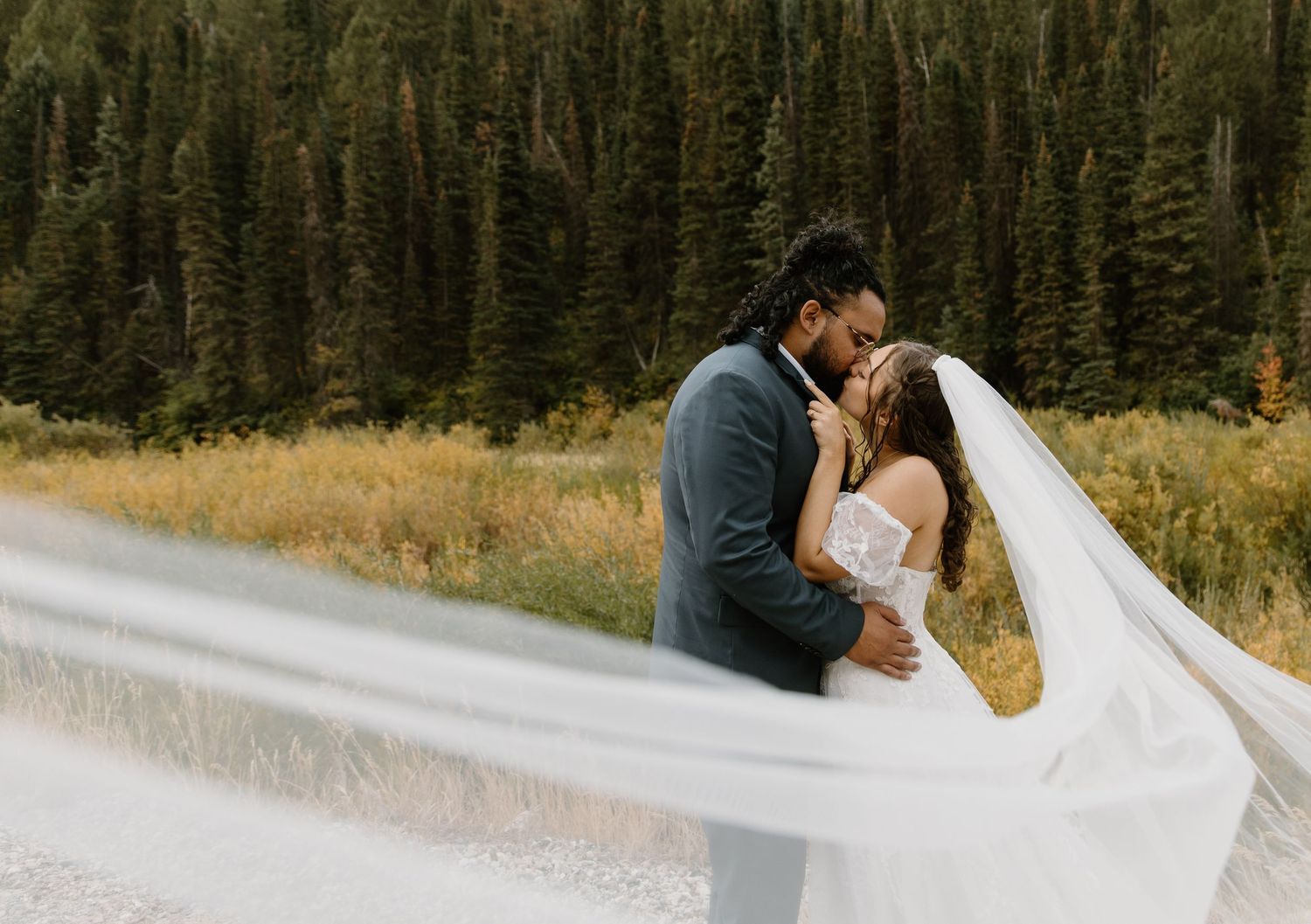 A romantic couple embraces in front of a scenic mountain forest backdrop during their wedding photo session.