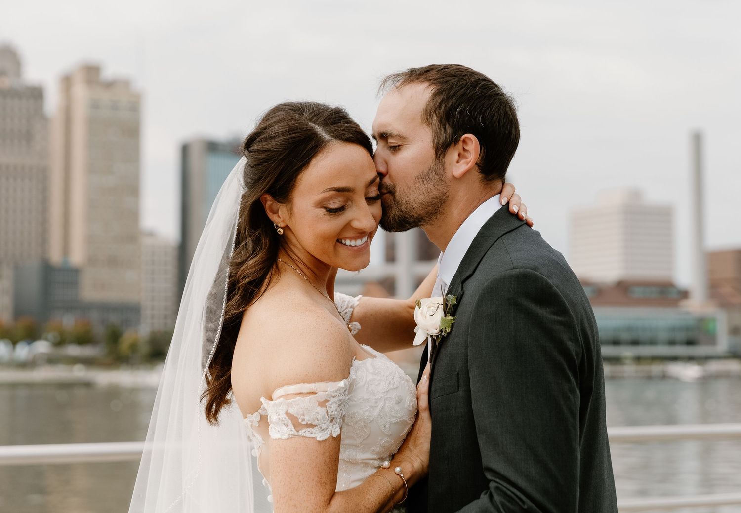 A romantic couple shares an intimate moment on their wedding day with a city skyline in the background.