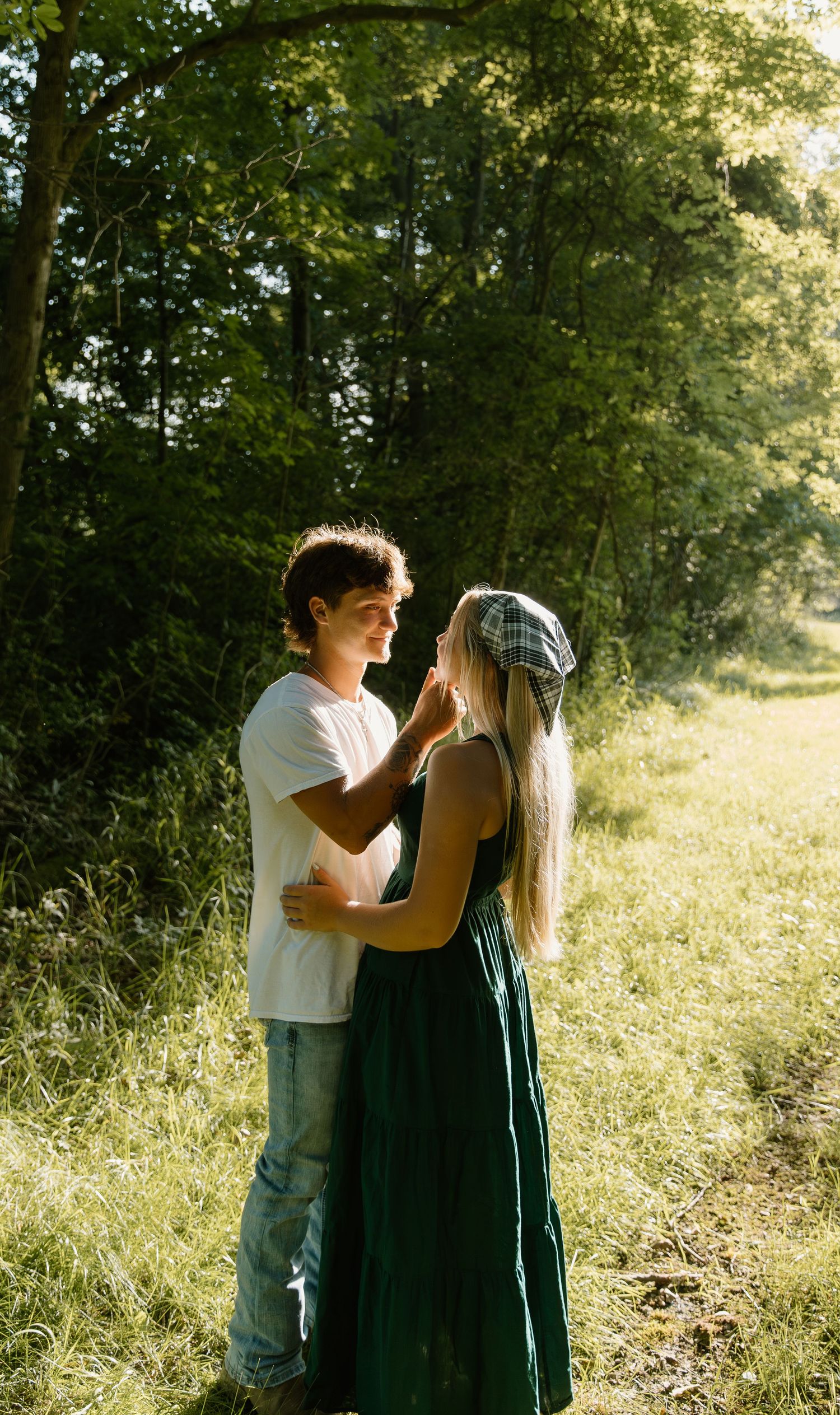 A romantic couple embracing on a sunlit forest path with her wearing a green dress and floral crown in Northwest Ohio.