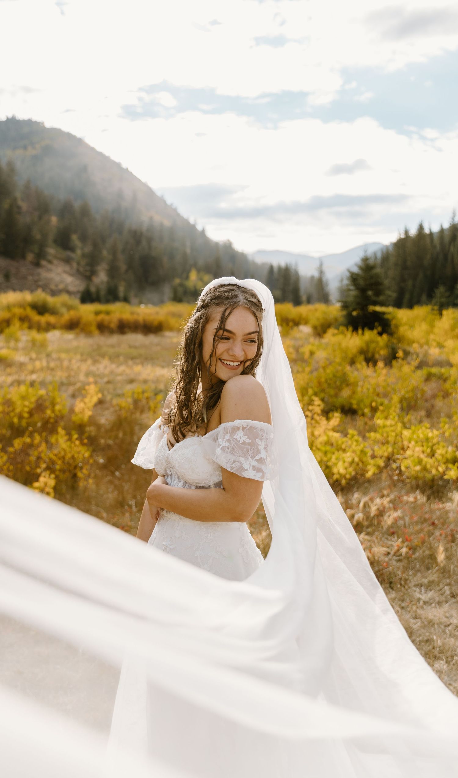 Bride in flowing white dress twirls joyfully in a mountain meadow with autumn colors.