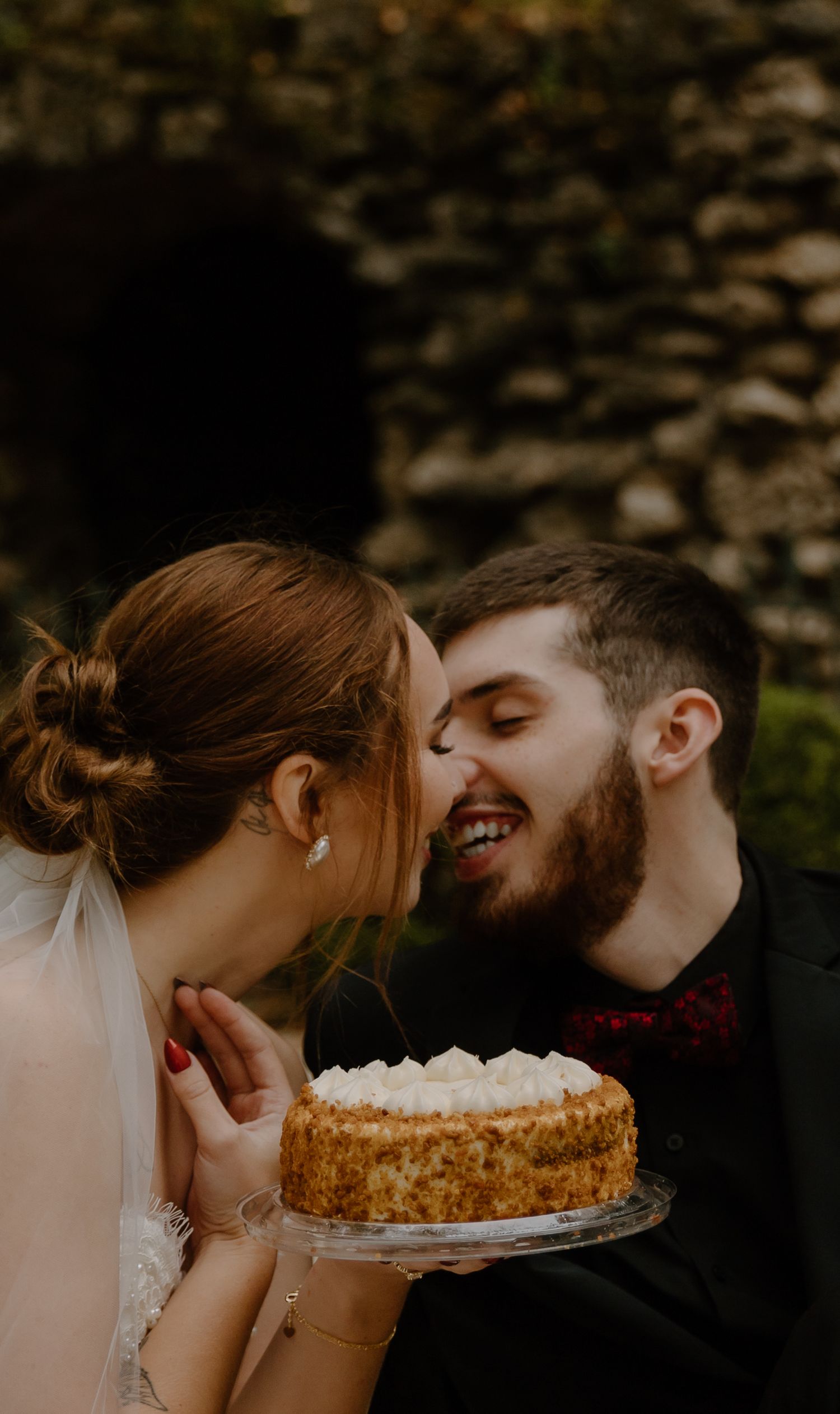 Playful elopement couple attempts to eat cake together in a romantic outdoor setting.