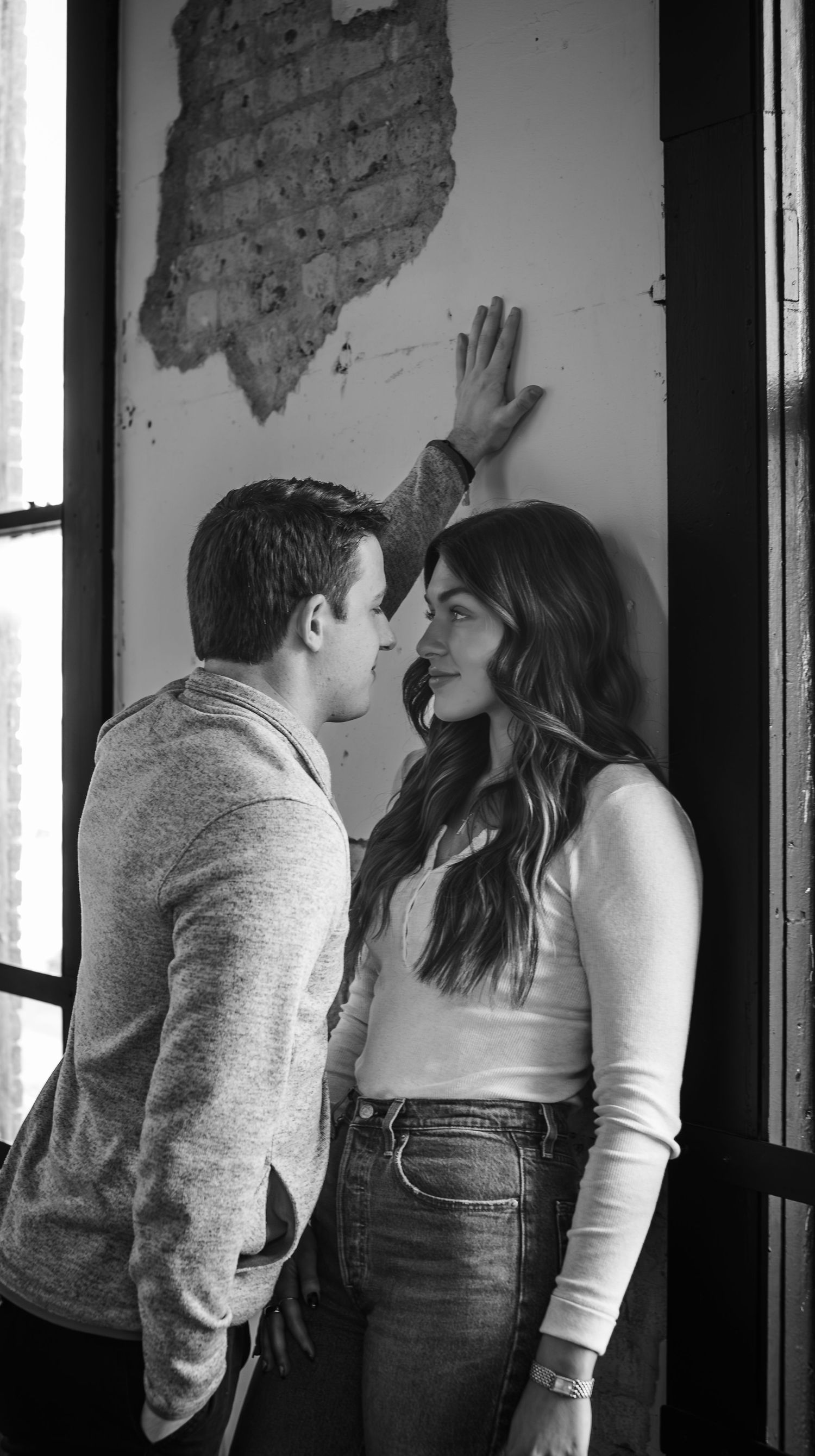 Black and white photo of couple sharing an intimate moment against industrial brick wall.
