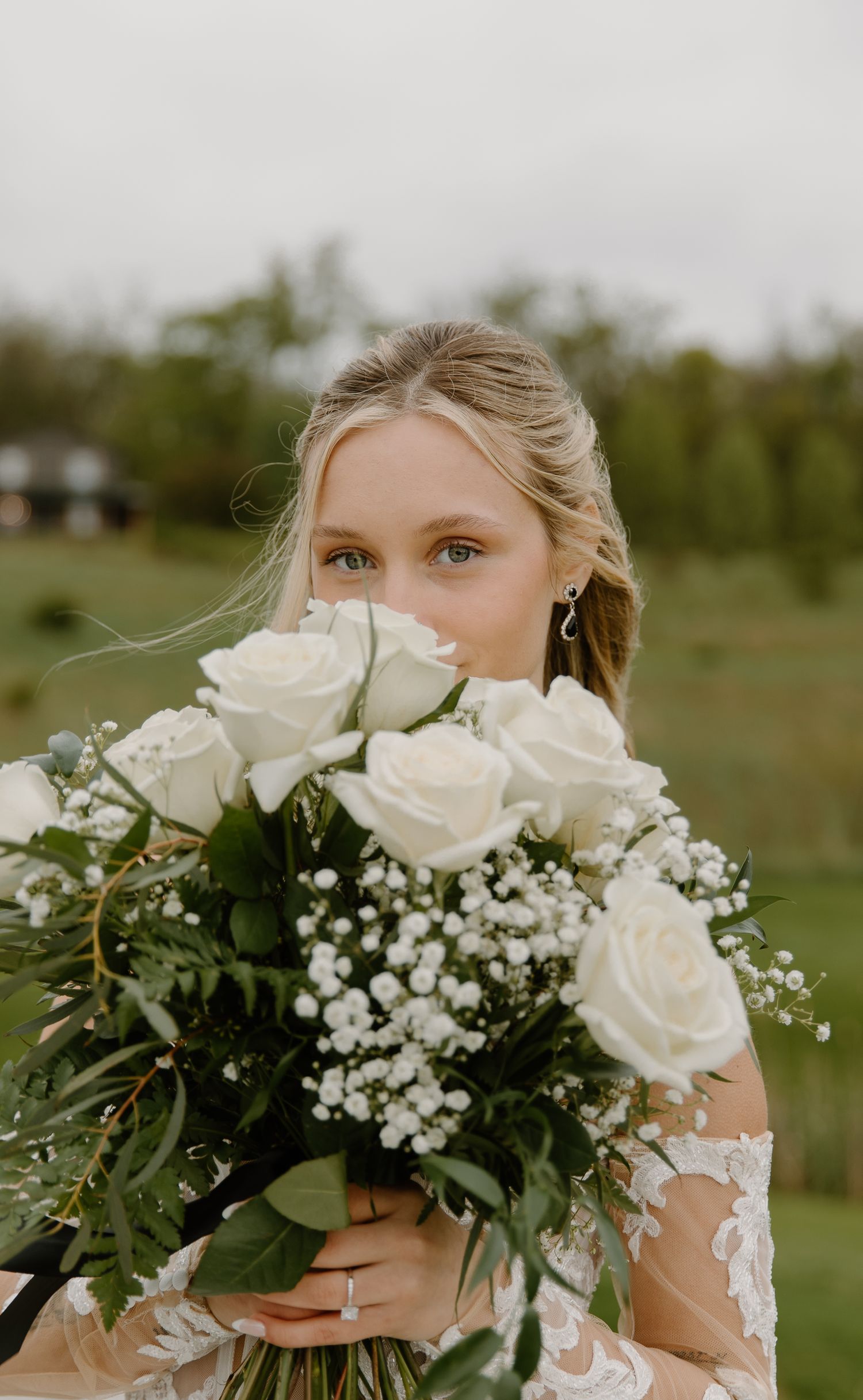Bride holds a bouquet of white roses and baby's breath at an outdoor wedding venue.
