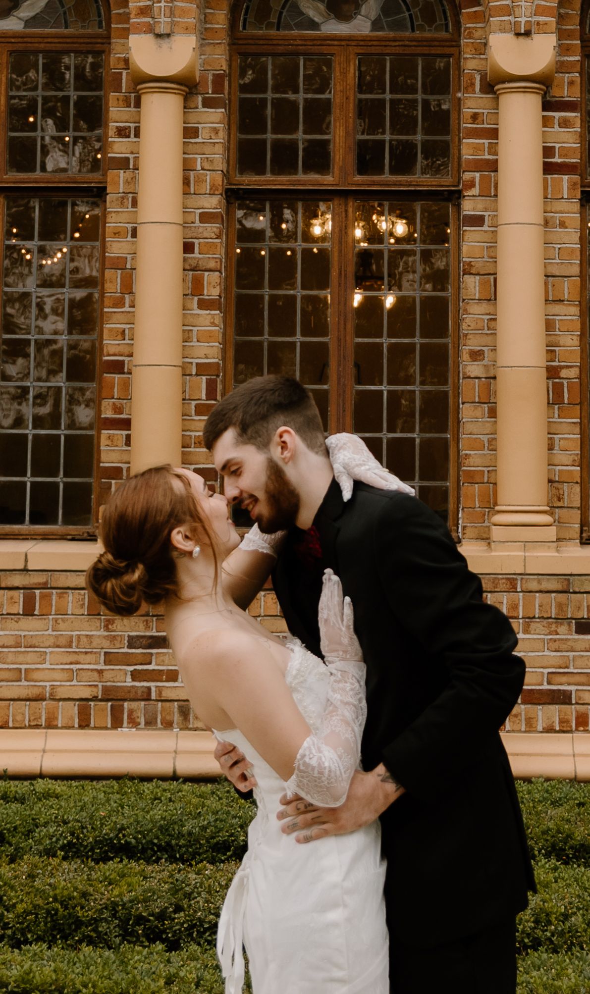 Intimate elopement couple sharing romantic moments in front of a brick building with arched windows.