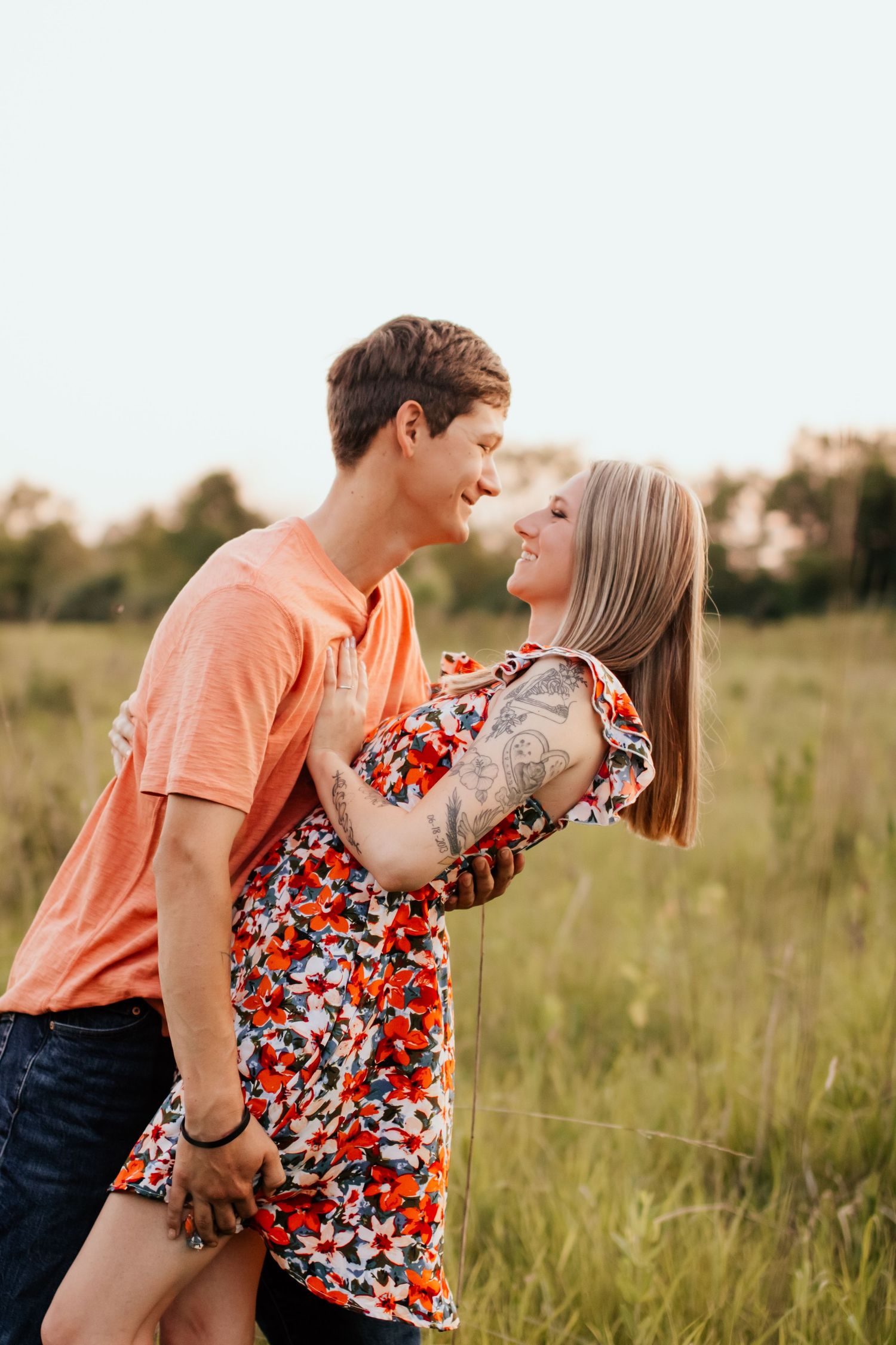 A couple shares a playful moment in a grassy field during summer.