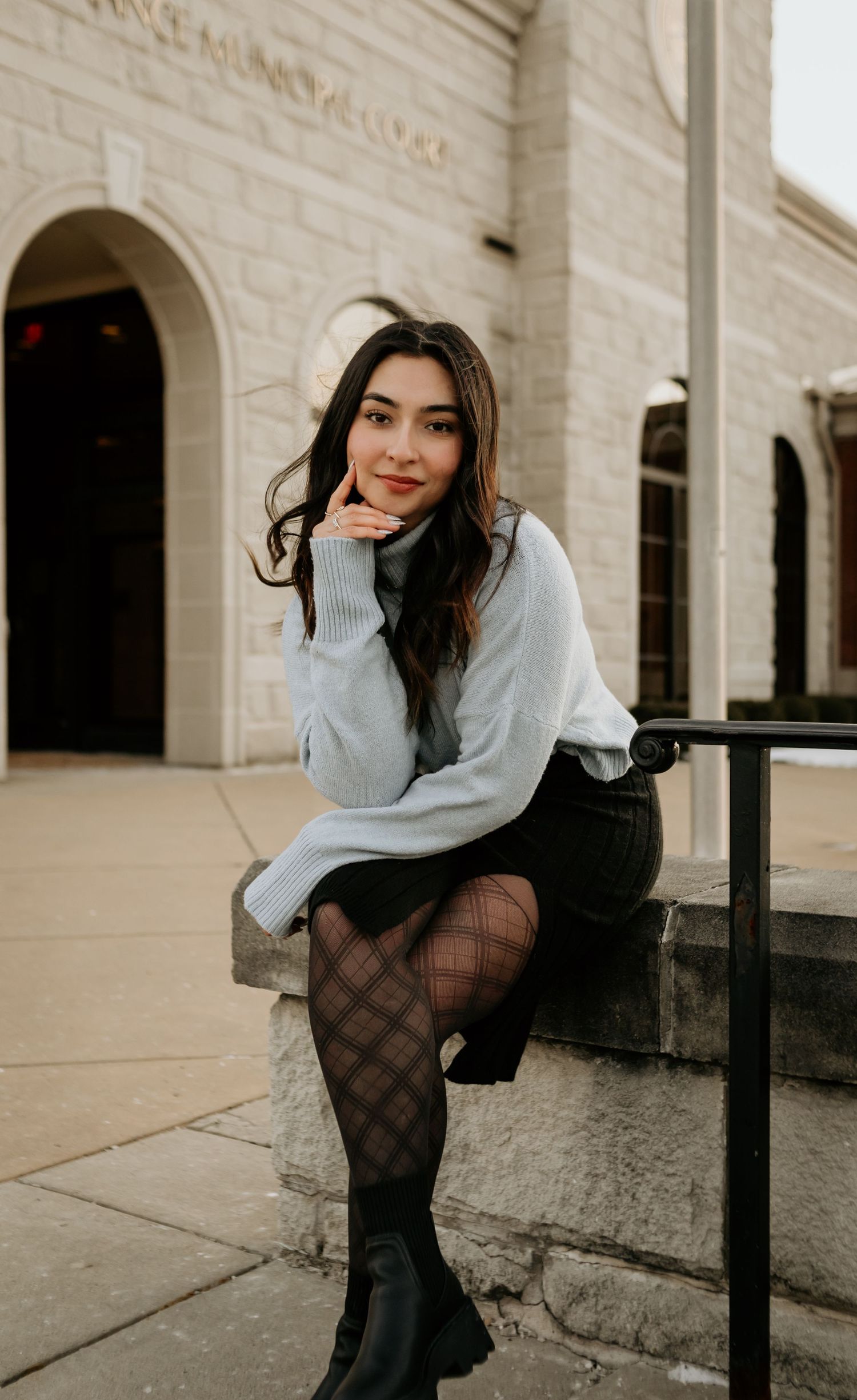 A fashionable winter outfit featuring a gray sweater, patterned tights and boots against a stone building backdrop.