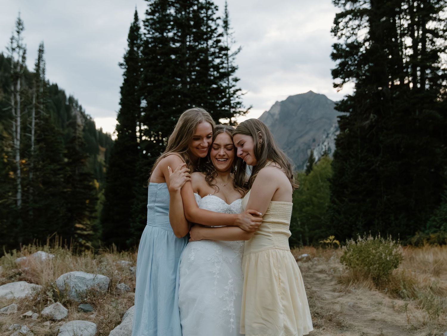 Wedding party embraces in front of mountain scenery at sunset in a rustic outdoor setting.