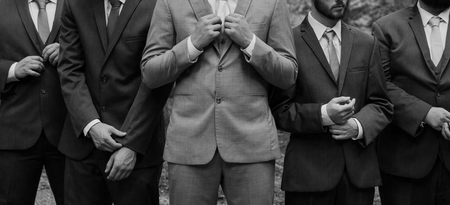 Black and white photo of three men in suits adjusting their jackets at a formal wedding event.