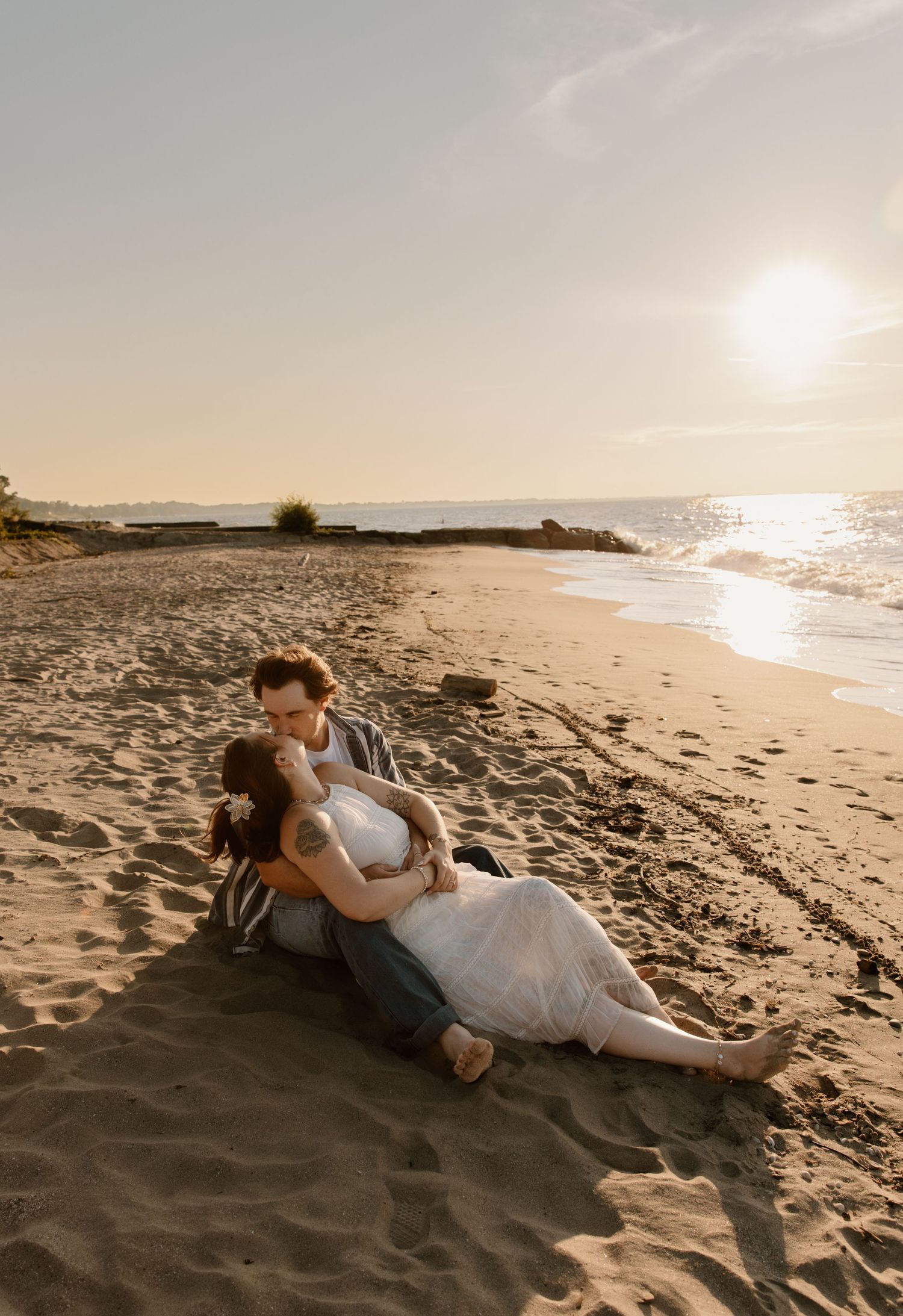 Couple in wedding attire sharing a romantic moment on a sandy beach at golden sunset.