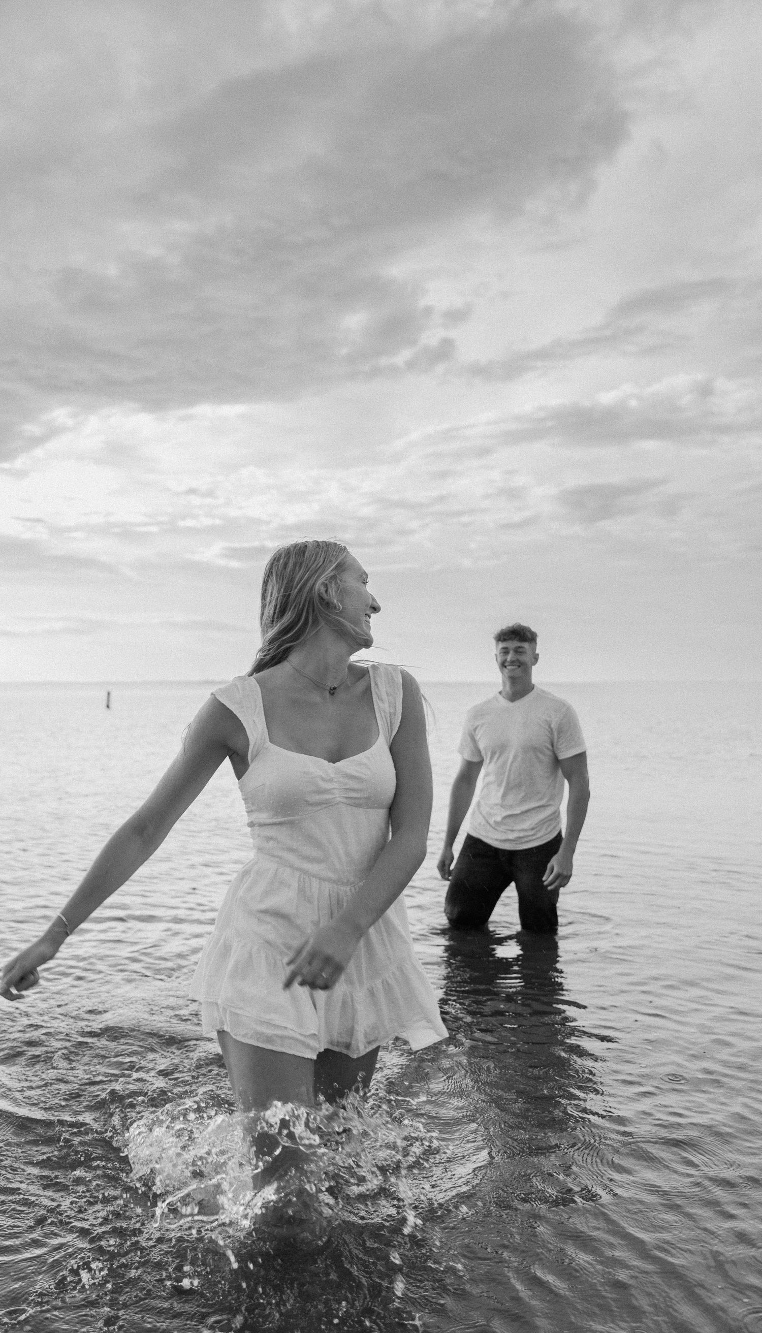 Black and white photo of two people having fun splashing in shallow ohio lake water under a dramatic cloudy sky at maumee bay state park.