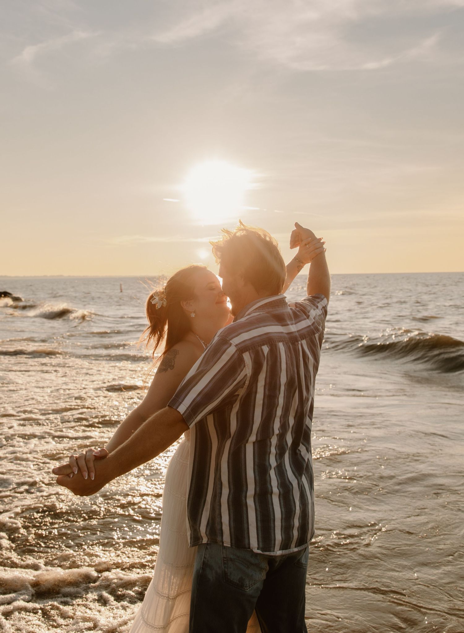 Couple dancing romantically on a beach at golden sunset with ocean waves in the background.