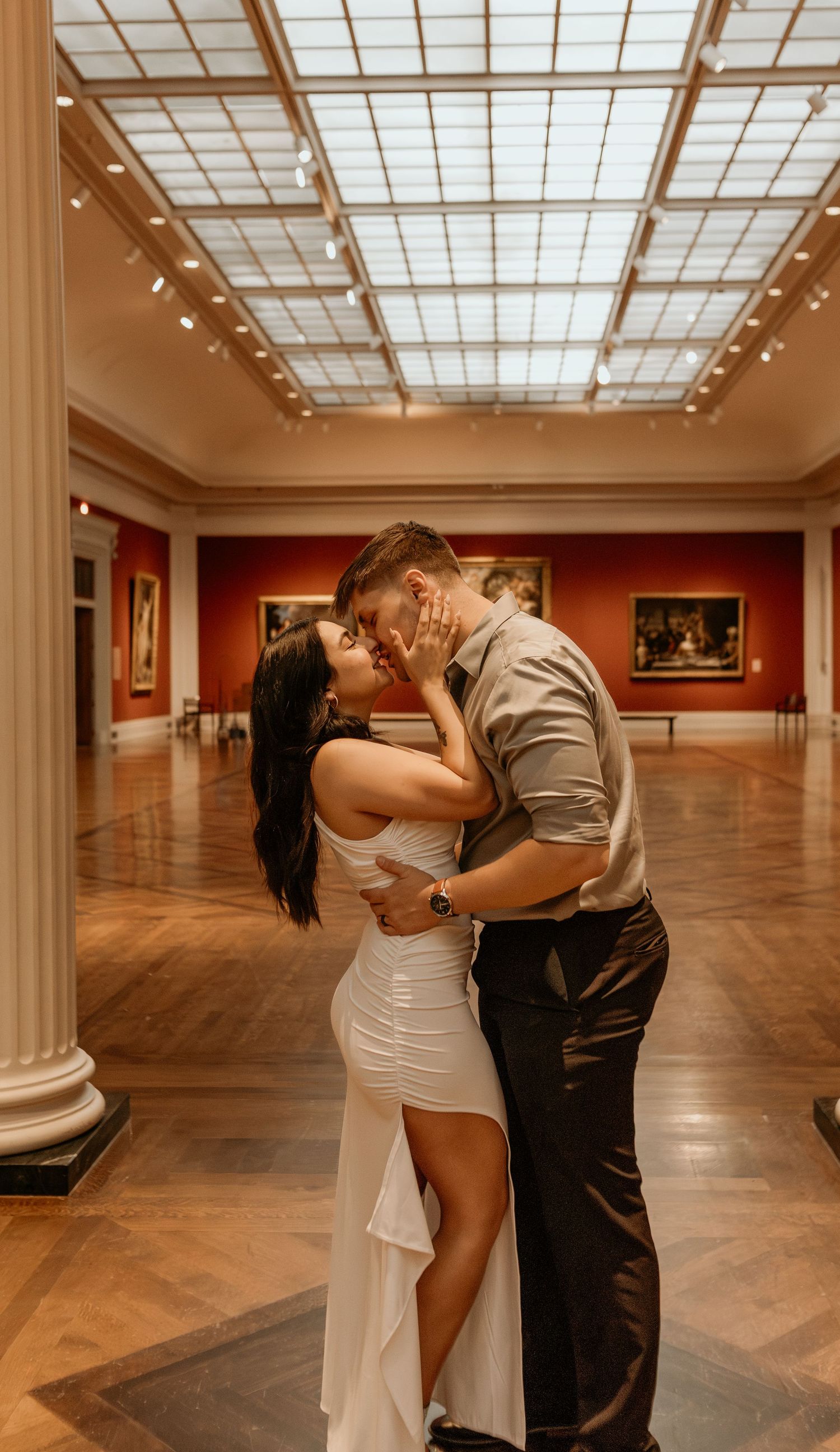 A romantic couple embraces in an elegant museum gallery with skylights.